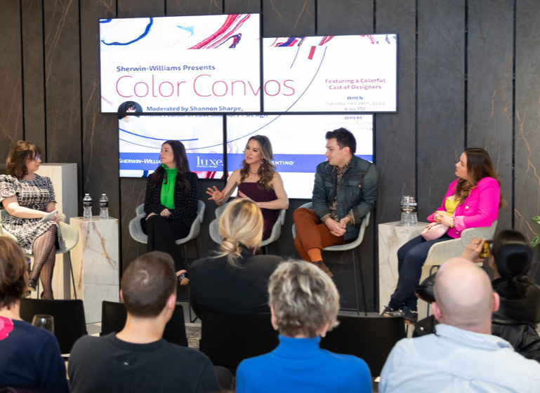 A panel discussion with five women and one man on a stage, with a large screen behind them displaying "Color Convos" and event details. The audience is seated facing the panel.