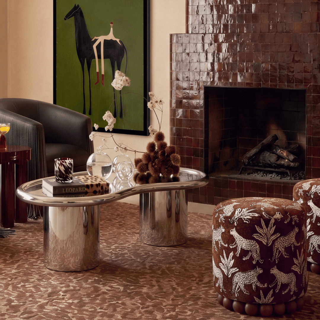 Eclectic living room with a plum brown tiled fireplace, chrome coffee table, abstract equestrian artwork, and animal-patterned stools.