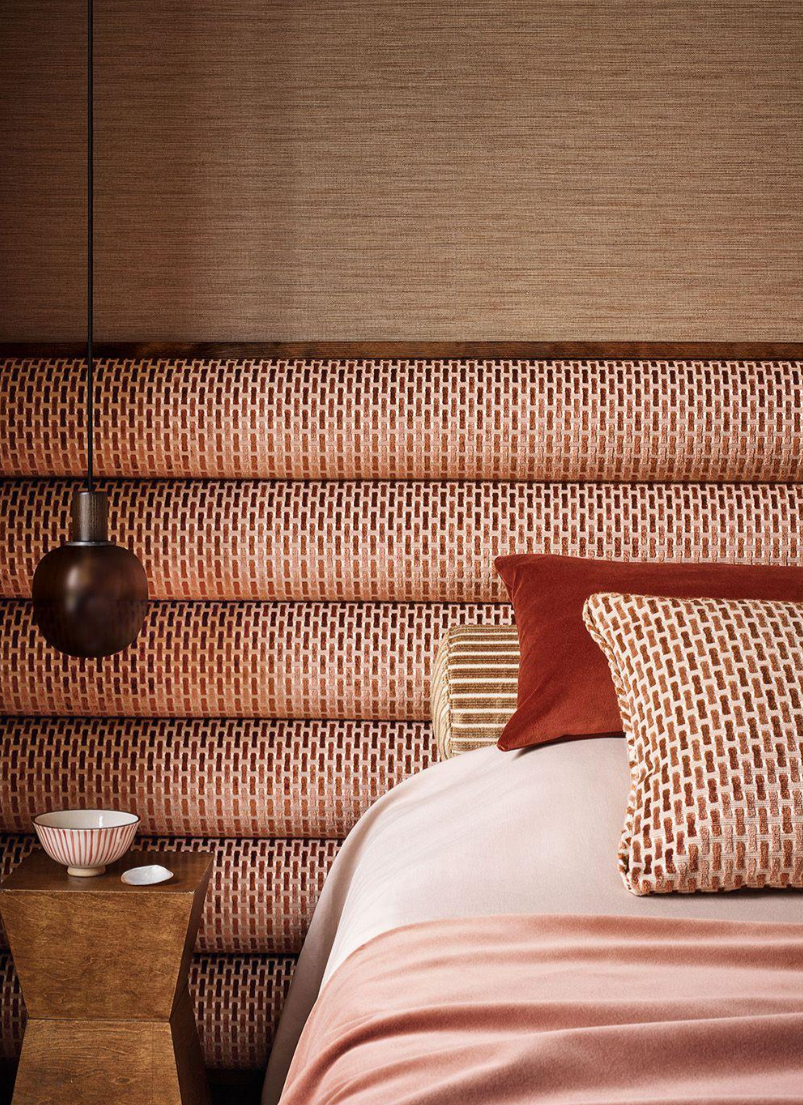 Layered bedroom featuring a patterned upholstered headboard, coordinating pillows, warm rust tones, a sculptural pendant, and handcrafted decorative accents.