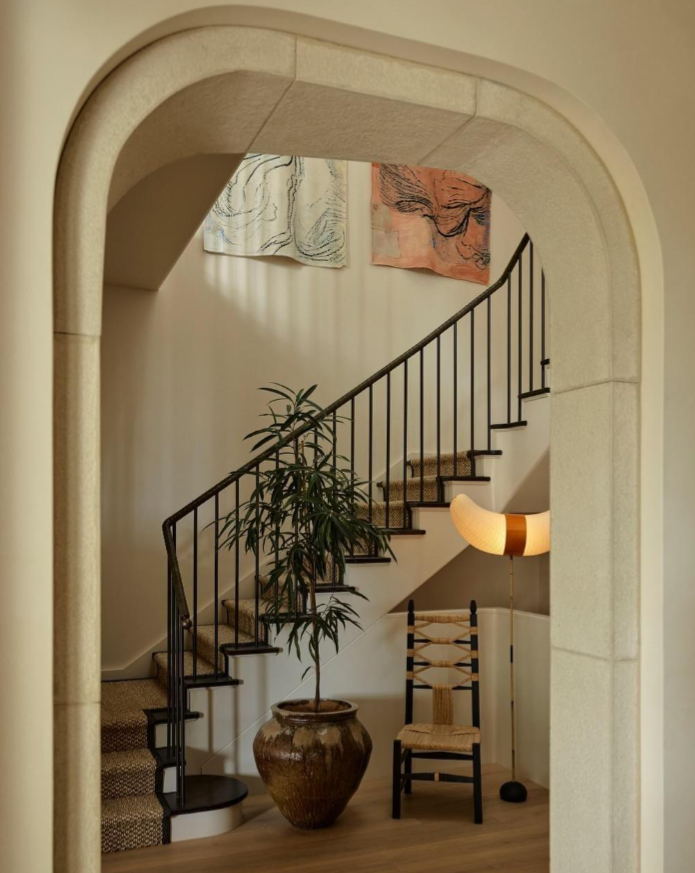 A black railing staircase with patterned carpet with a horn shaped floor lamp and detailed archway