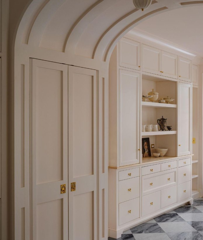 Arched hallway featuring custom white millwork, concealed storage, inset display shelves, brass hardware, and a graphic marble floor.