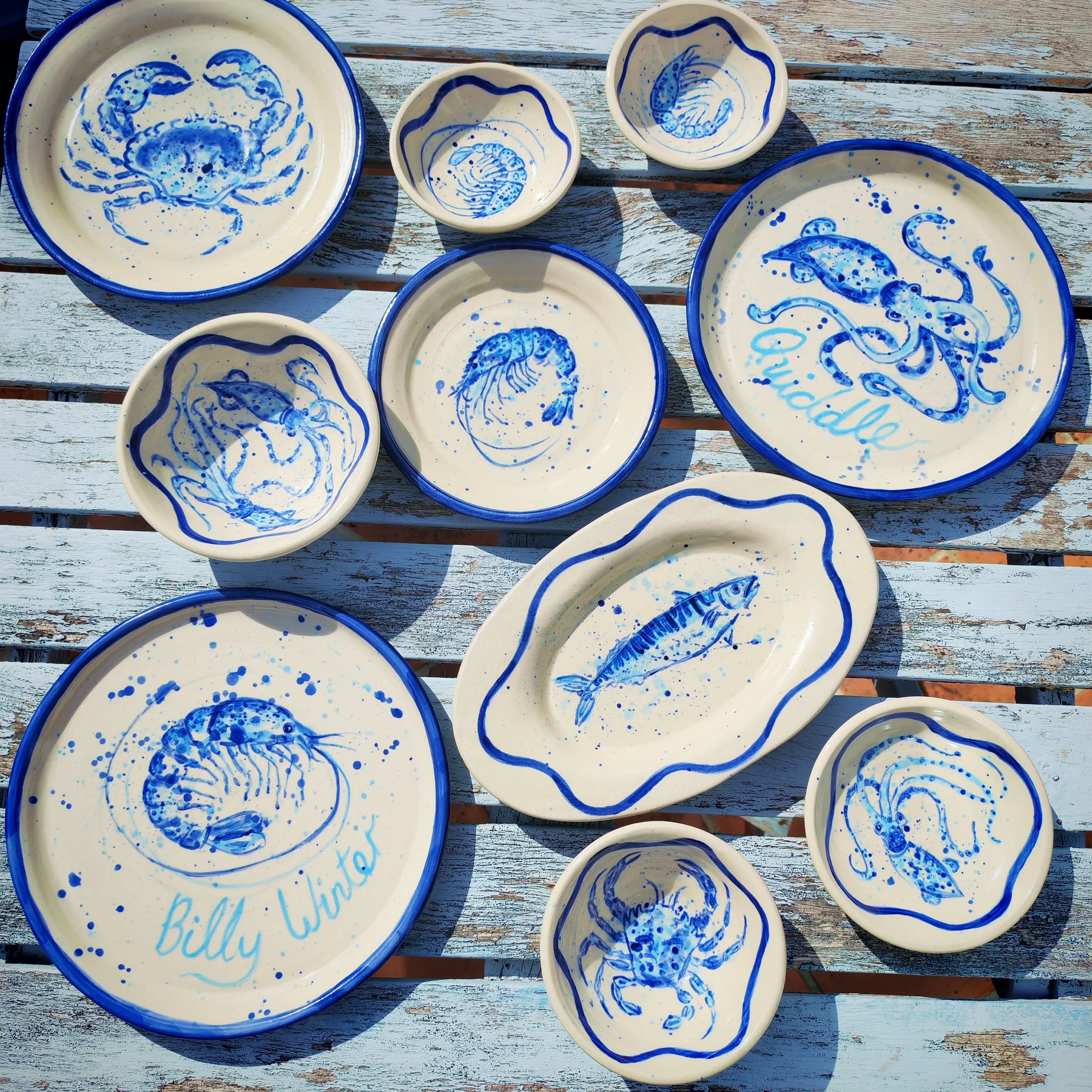 Collection of ceramic plates and bowls with blue painted jellyfish and marine life designs on a weathered wooden surface.