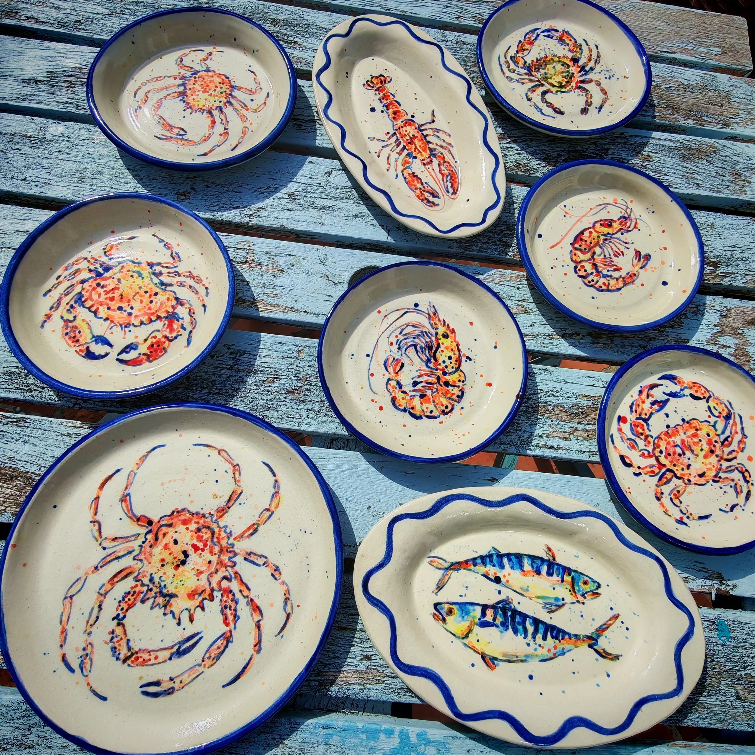 Ceramic bowls and a ceramic tray with painted images of lobsters, crabs, and fish on a weathered wooden surface.