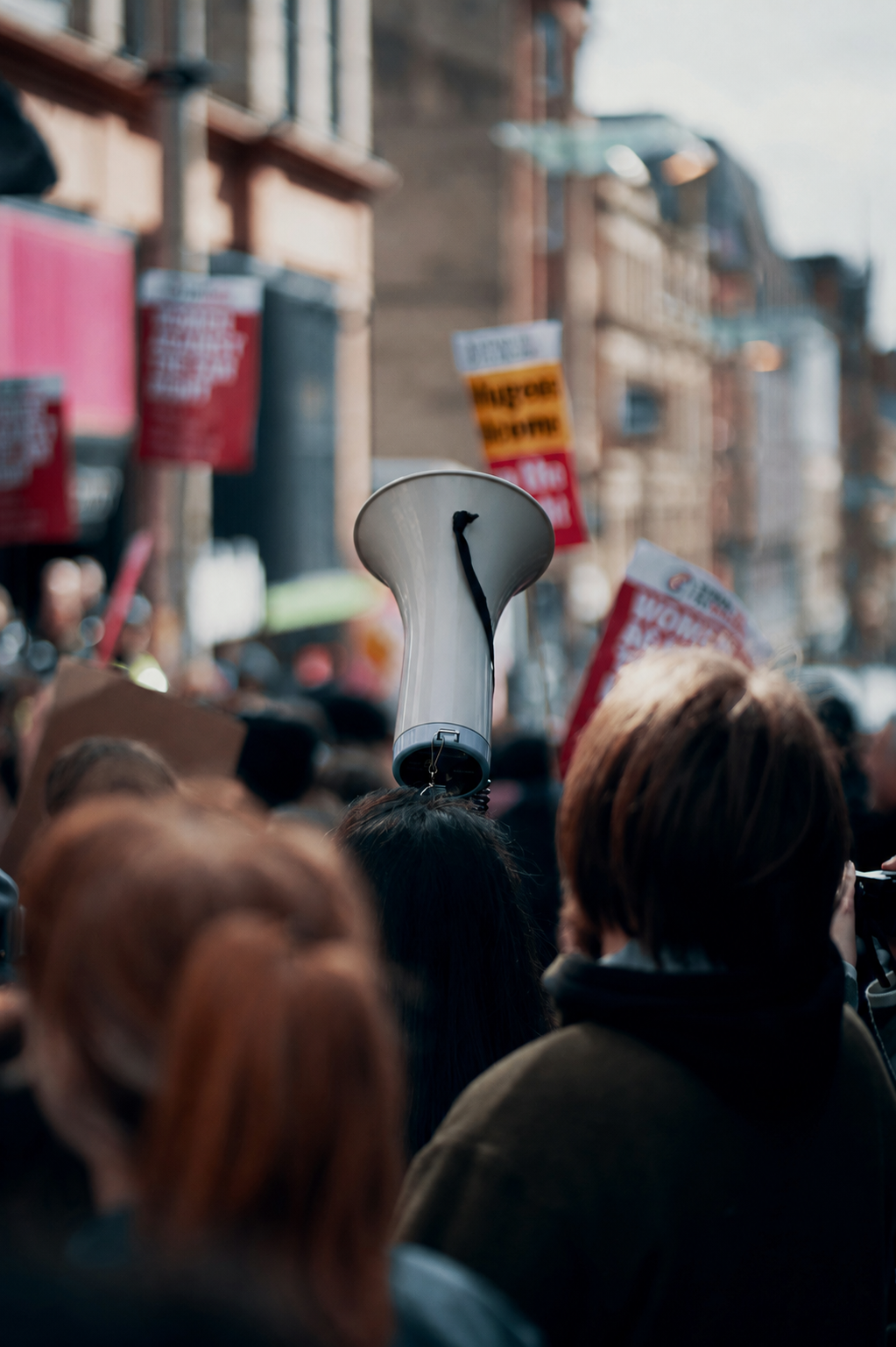 Crowd of protesters holding signs, with a person holding a megaphone in the center during a demonstration on a city street.