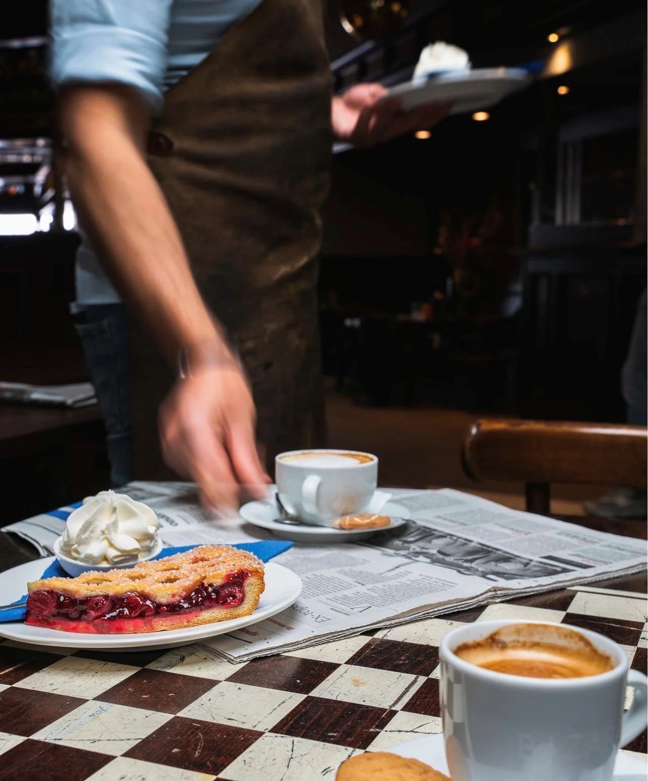 Een kop koffie, een stuk kersenvlaai met slagroom en een kopje koffie op een tafel in een café of restaurant.