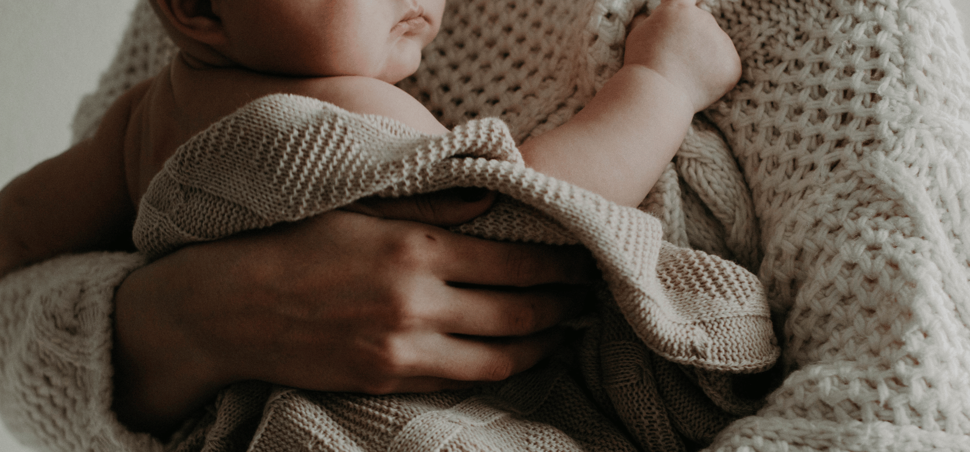 Close-up of a baby being gently held, wrapped in knitted blankets with textured patterns.