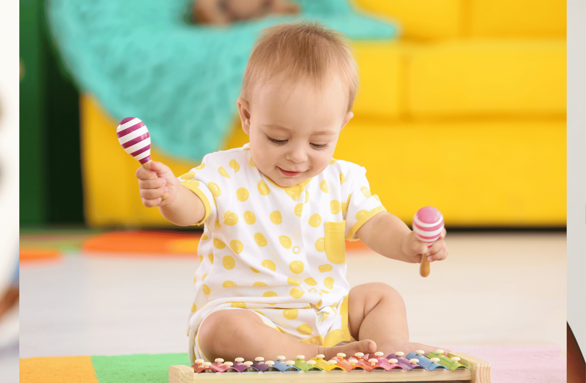 A young child with light hair wearing a white shirt with yellow polka dots is sitting on the floor with legs crossed. The child is playing with a rainbow-colored xylophone and holding two maracas, one in each hand. The background features a blurred yellow and green room, indicating a colorful play area.