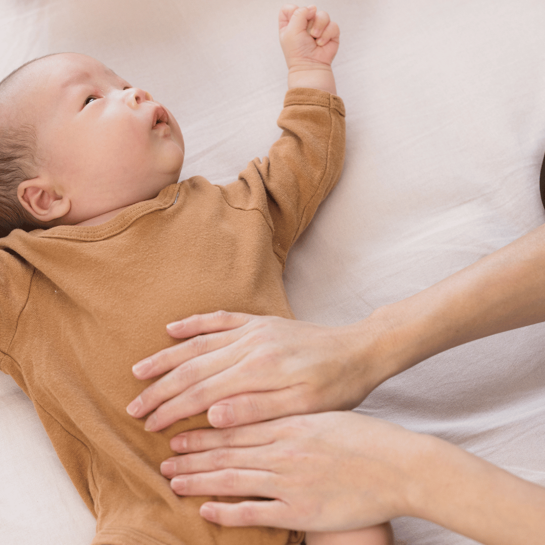 A young child lying on a bed with an adult's hands placed on their stomach for a check-up or examination.
