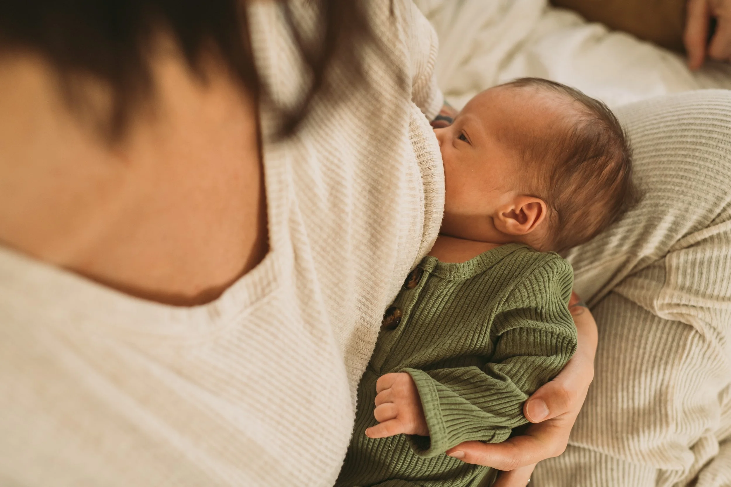 A mother breastfeeding her baby while lying on a bed, with her hand gently holding the baby's arm.