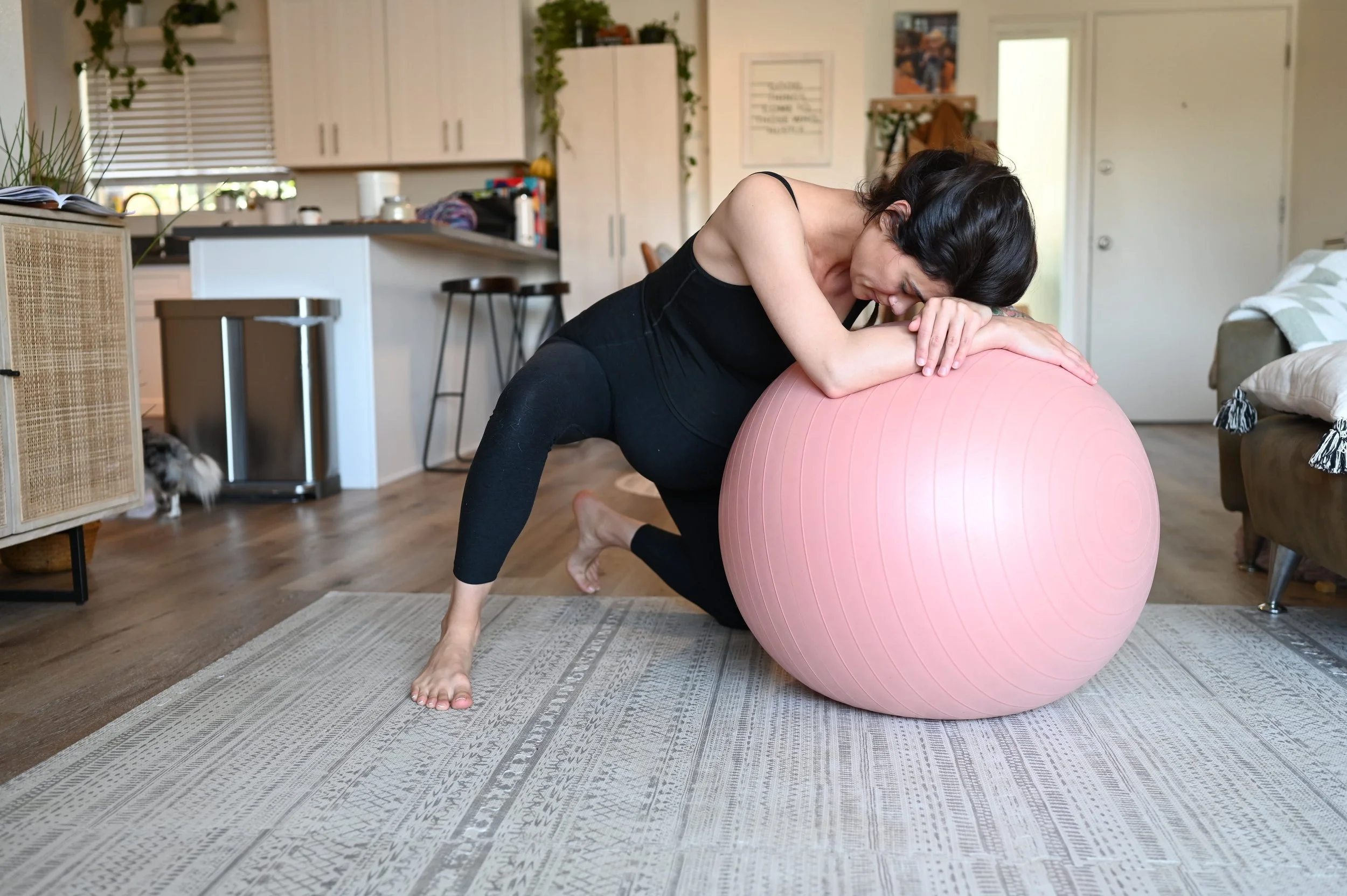 Woman doing a plank exercise on a pink exercise ball in a living room.