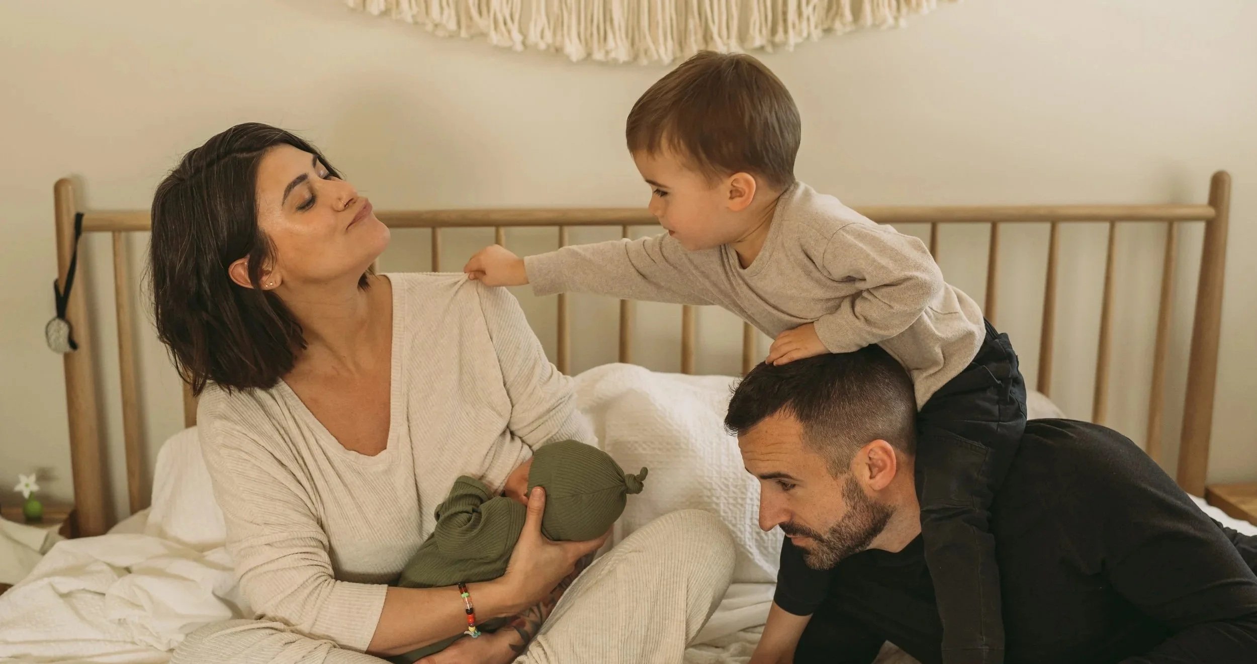 A woman holding a baby with a man and a young boy on a bed, all smiling and engaging with each other in a cozy bedroom.