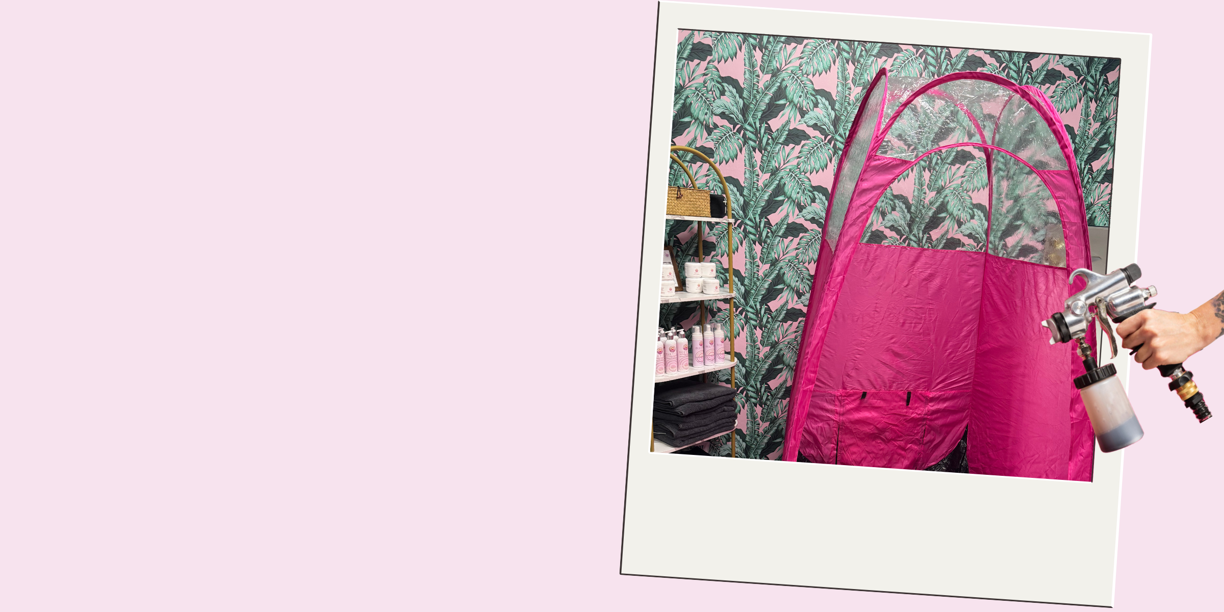 A person holding a spray gun in front of a mirror with a pink tent setup, against a tropical leaf wallpaper background, in a retail or display setting.