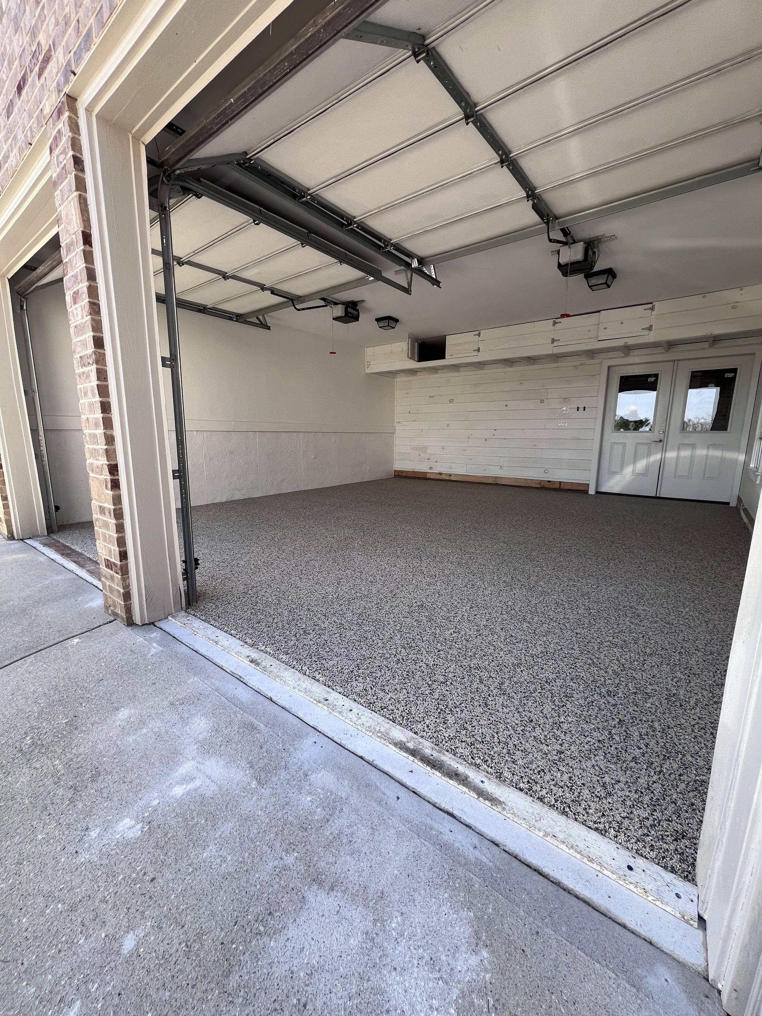 Open garage with partially raised garage door, showing the interior with white walls and resin-bound pebble garage flooring designed and installed by Pebble & Resin Co