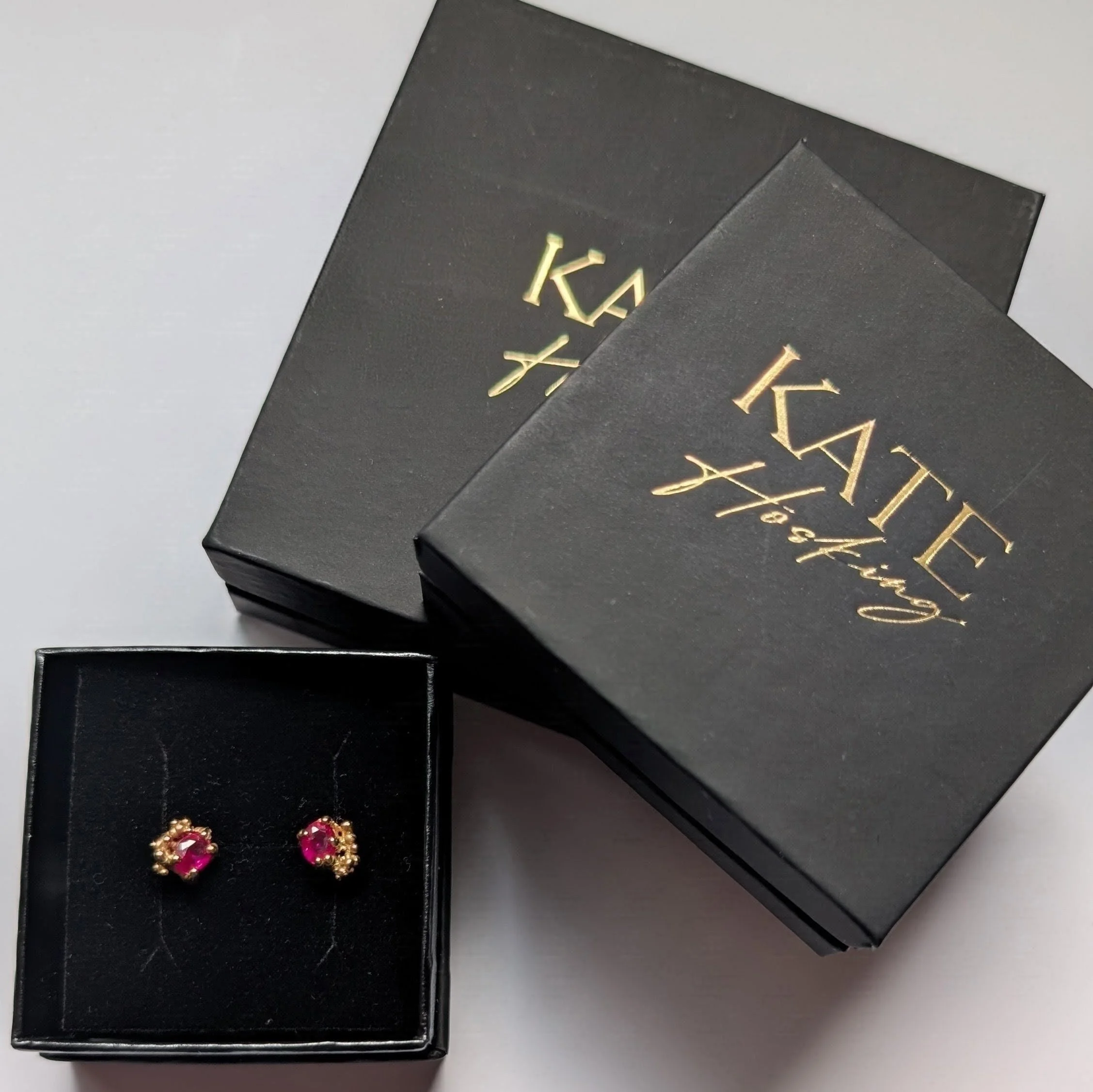 Pair of earrings with pink gemstones and gold accents displayed in a black jewelry box.