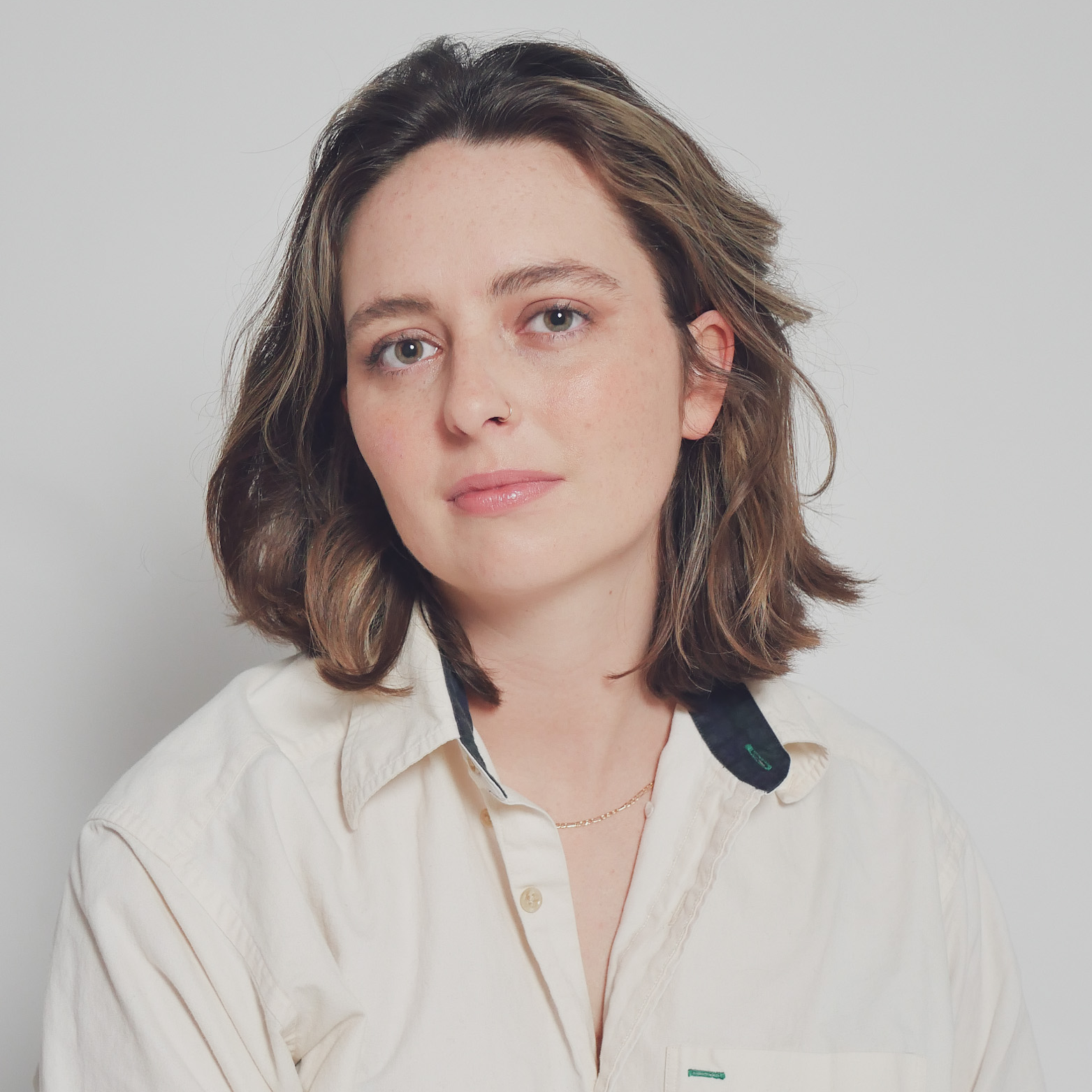 Headshot of Maggie Boyd Hare owearing a cream-colored button-up shirt and a delicate gold necklace, standing against a plain white background.