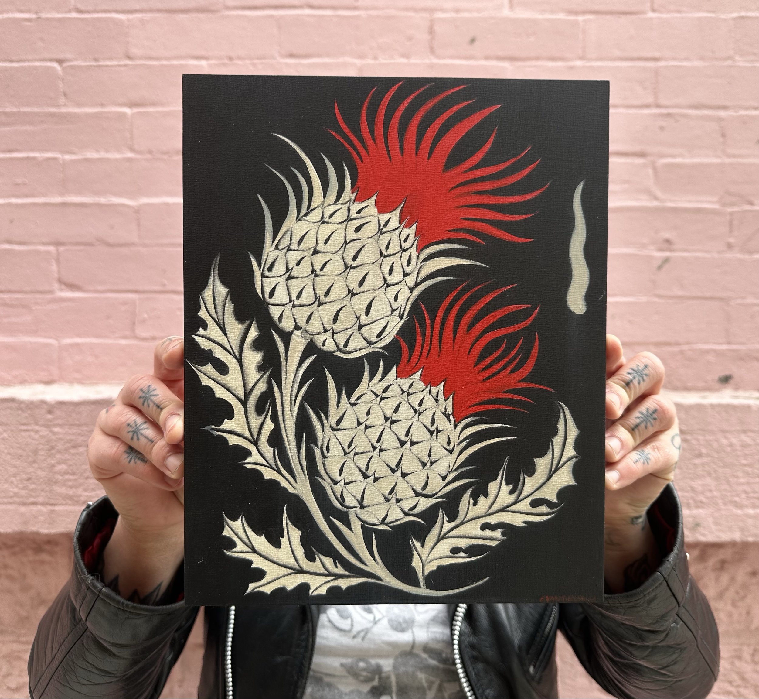 A person holding a black poster with a stylized white and red pineapple illustration in front of a pink brick wall.