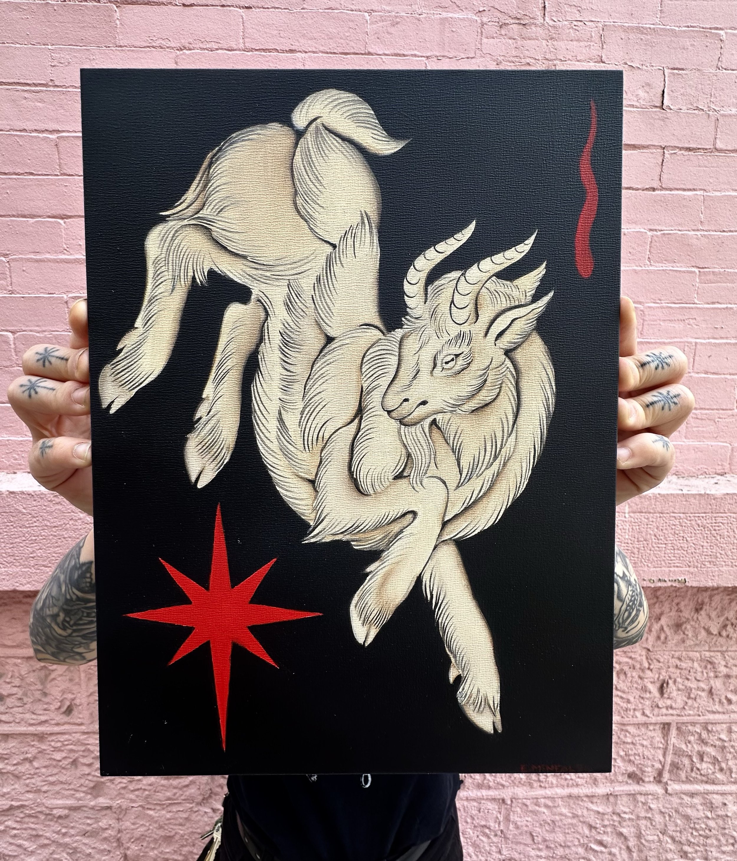 A person holding a black canvas with an autumn-colored tiger illustration against a pink brick wall. The tiger is white with detailed fur lines, and there are red elements, including a star and a wavy line, on the canvas.