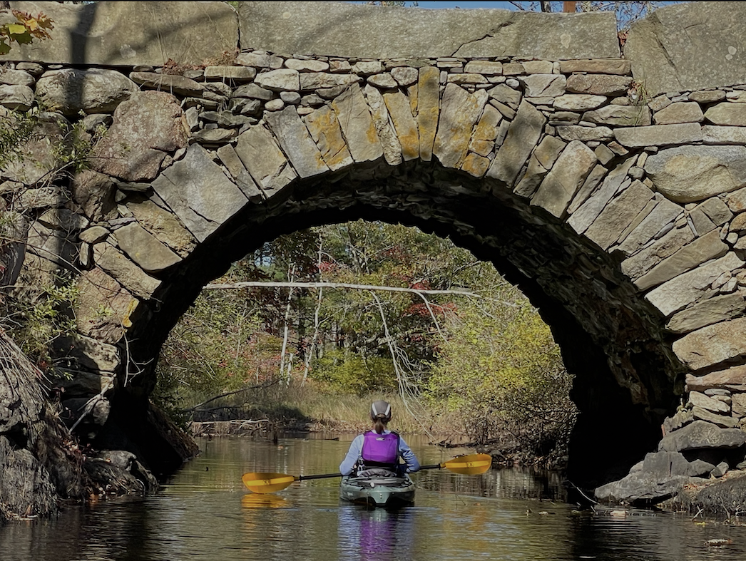 woman kayaking on a river under a stone bridge