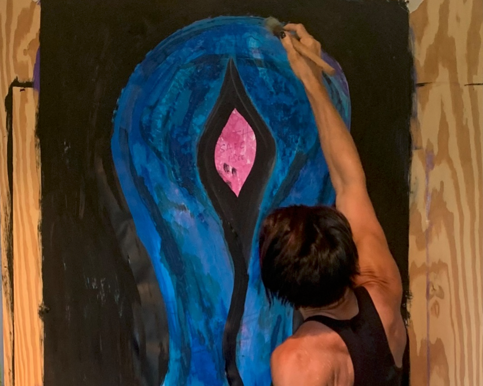 Person painting an abstract artwork featuring shades of blue, black, and pink on a large vertical canvas.
