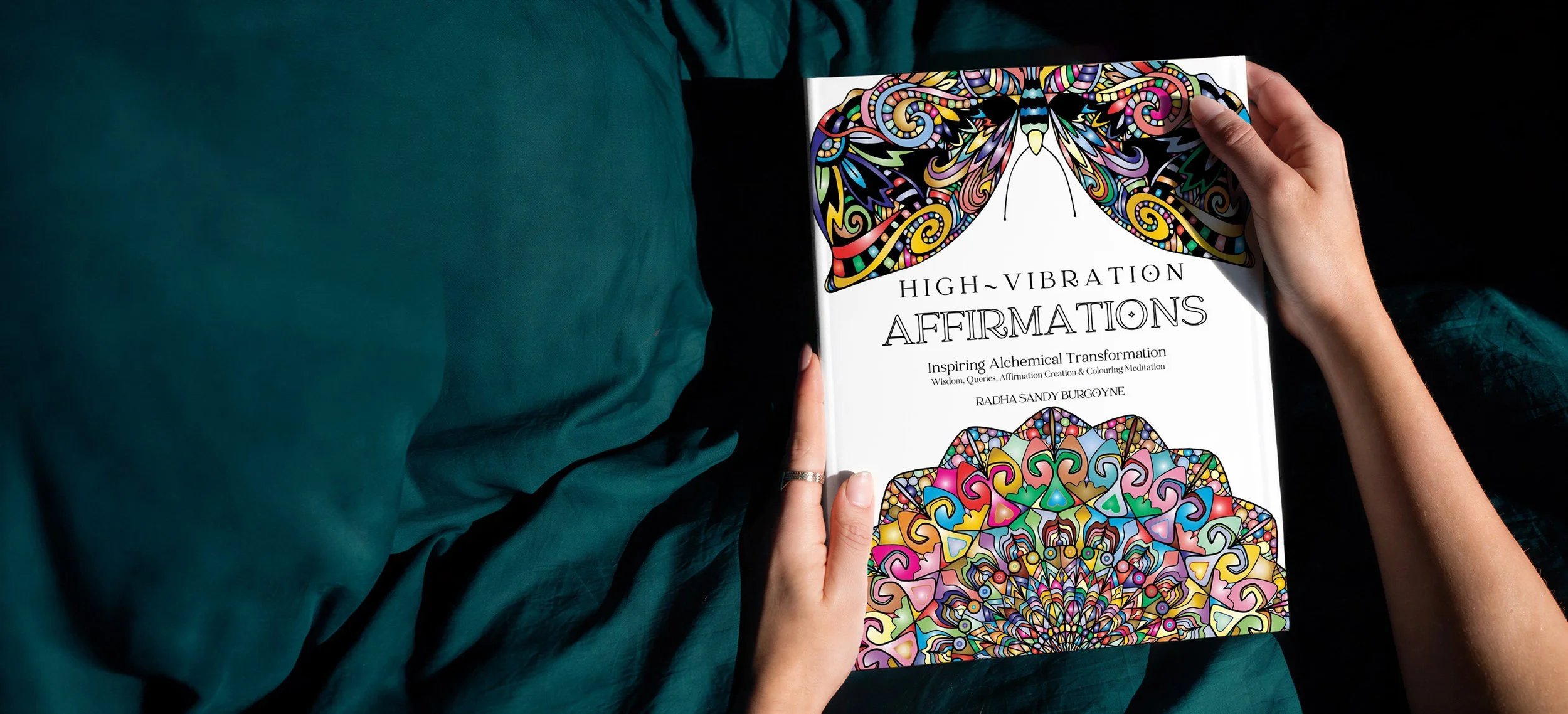 Person holding a book titled 'High-Vibration Affirmations' with colorful, intricate mandala and abstract designs on the cover.