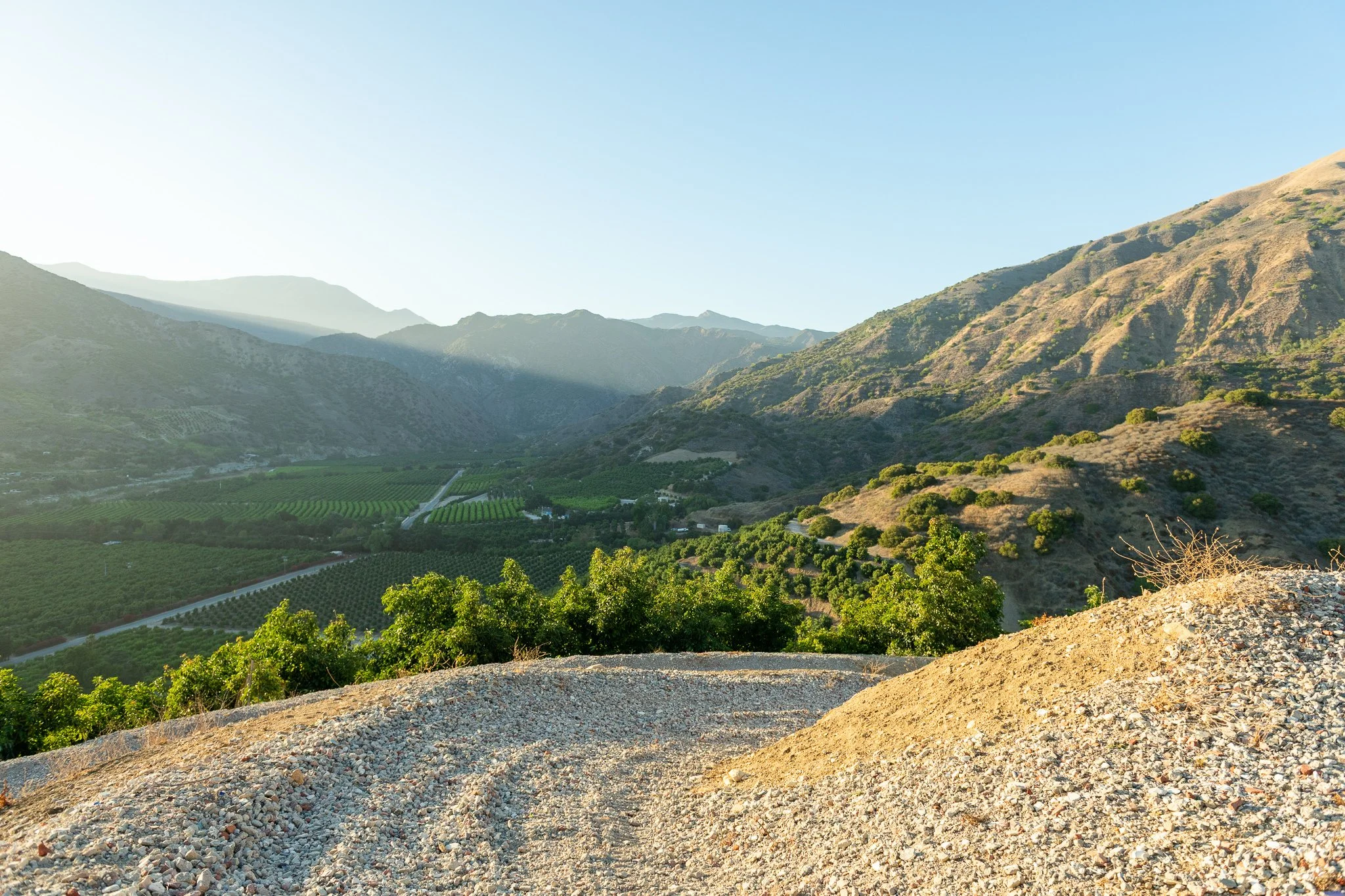 Open landscape with hills and mountains, some greenery and farmland at the base, under a clear blue sky.