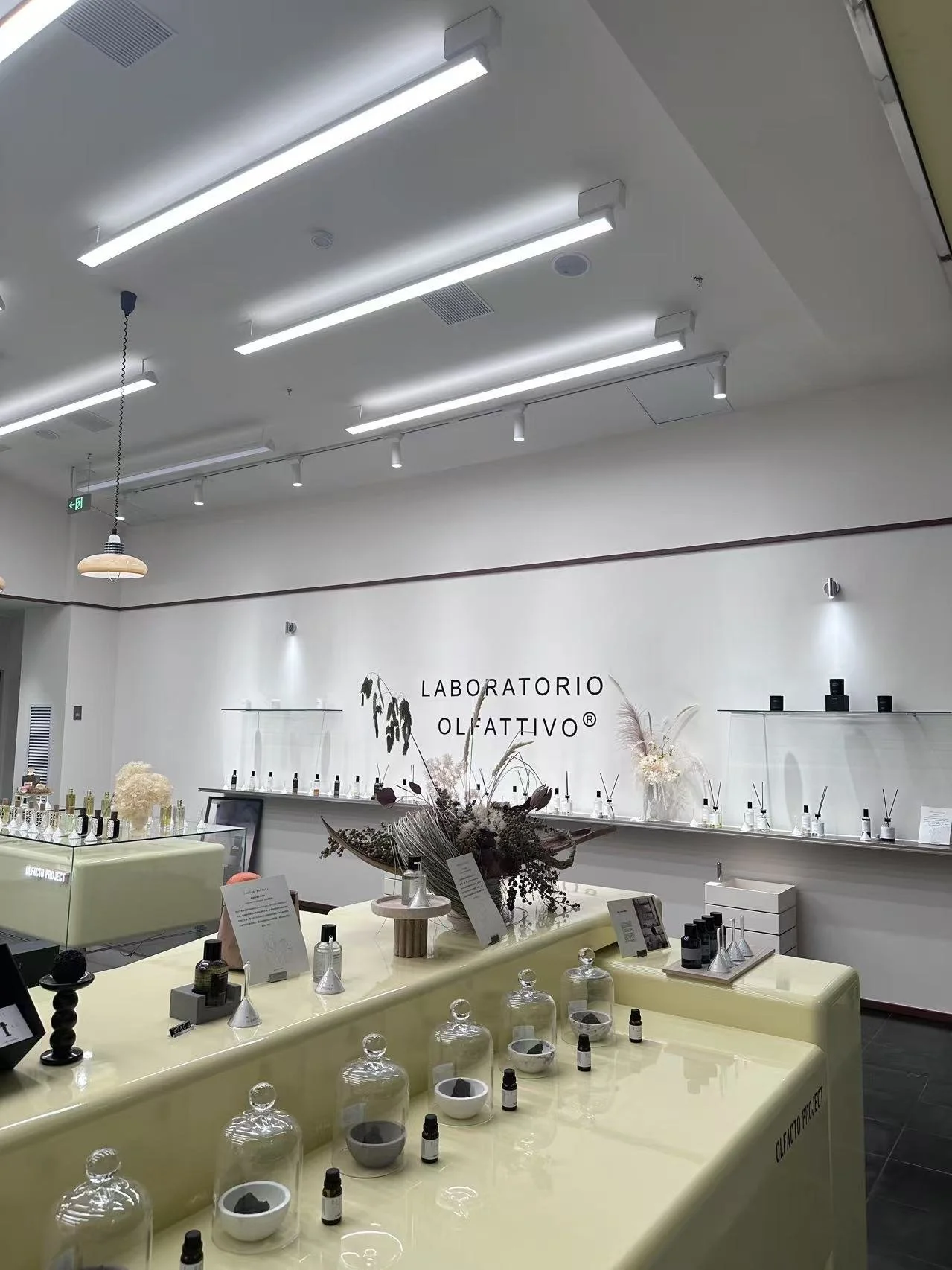 Interior of a modern perfume store with the sign 'Laboratorio Olfattivo', displaying various perfume bottles and fragrance samples on tables and shelves, with decorative floral arrangements.