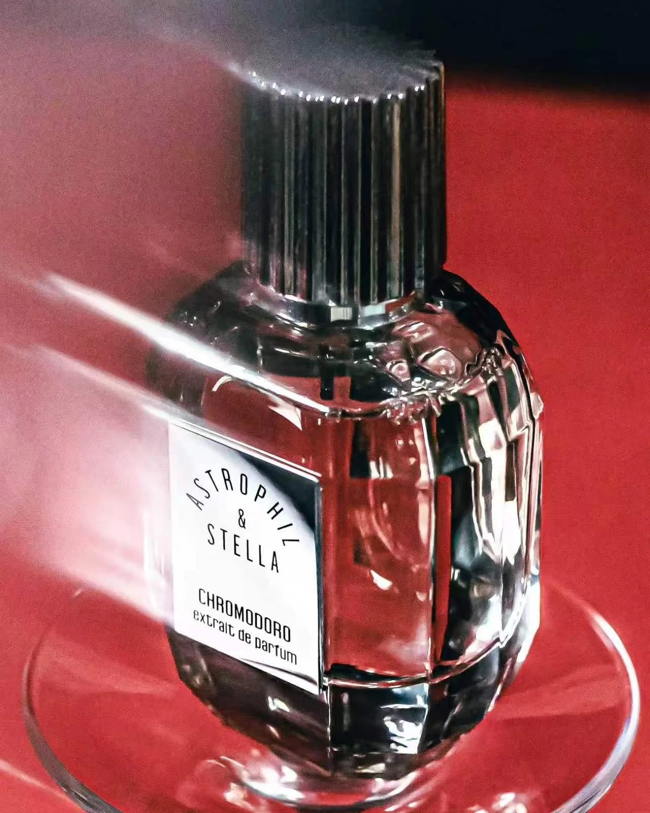 A glass perfume bottle with a silver cap, labeled "Astrophil & Stella," resting on a red surface.