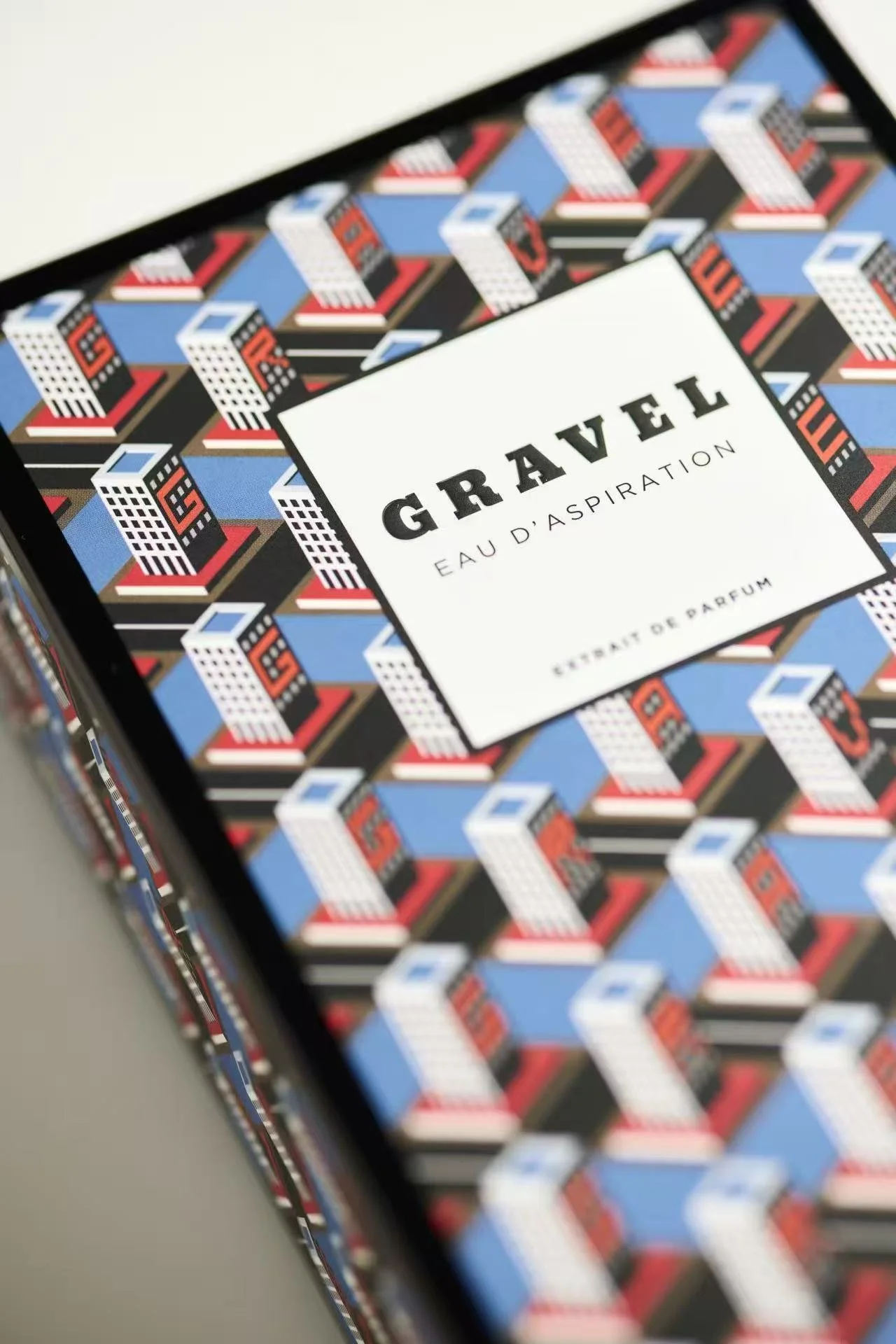 Close-up of a box of GRAEL Eau d'Aspiration perfume, with a colorful, geometric cityscape pattern on the packaging.