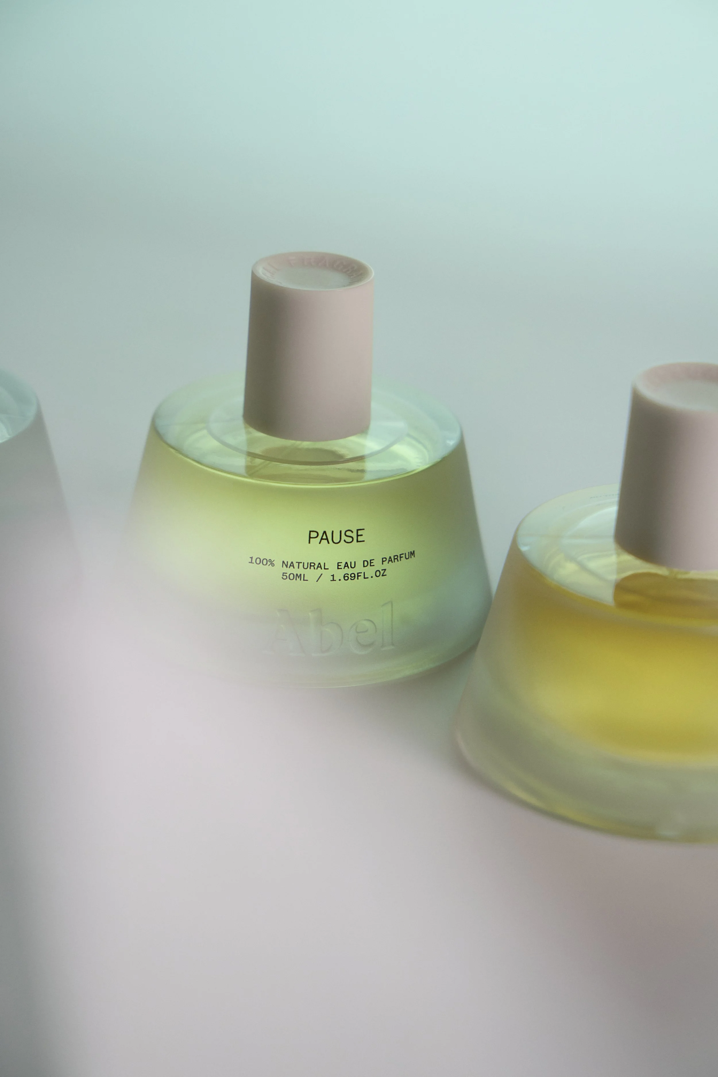 Close-up of pastel-colored perfume bottles with round caps and labels, set against a white background.