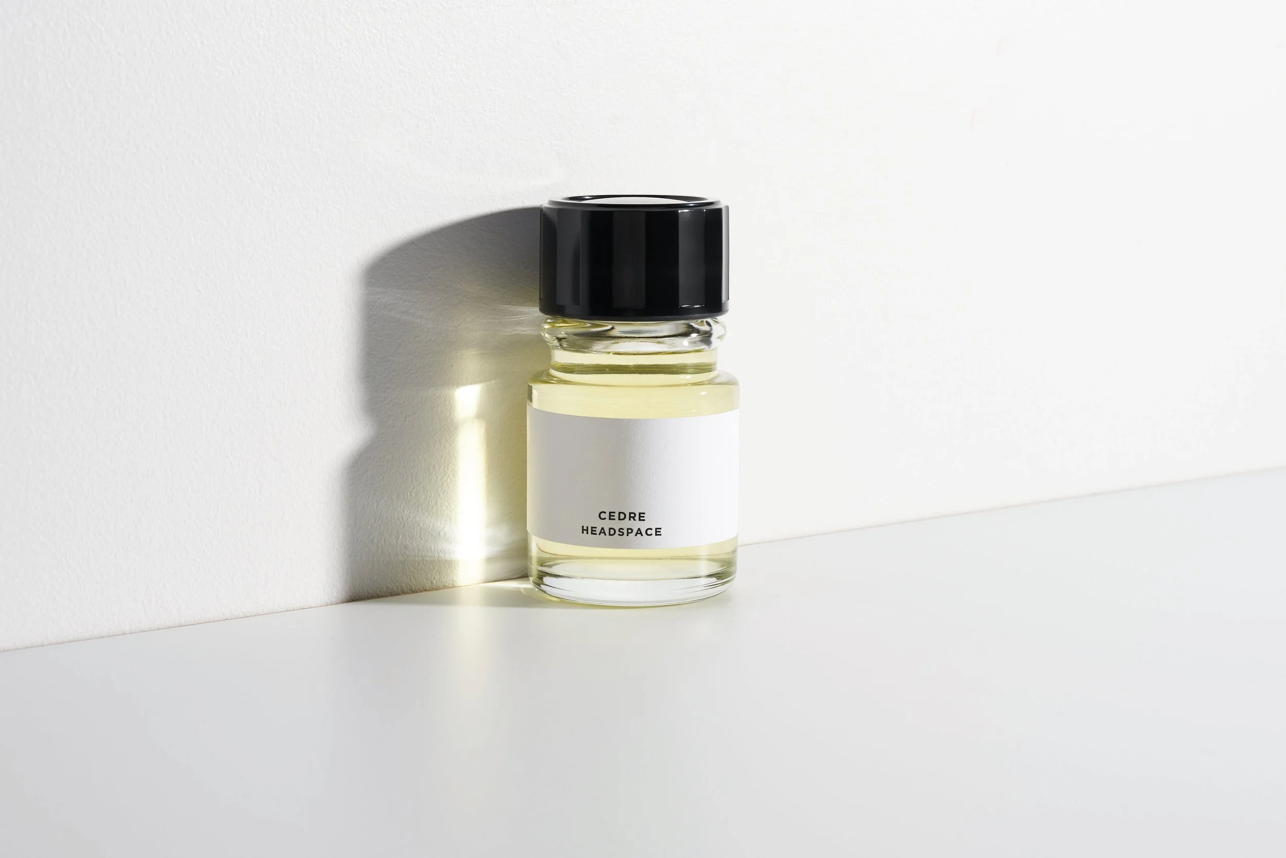 A small bottle of Cedre Headspace perfume with a black cap, placed on a white surface with a plain white background, casting a soft shadow.