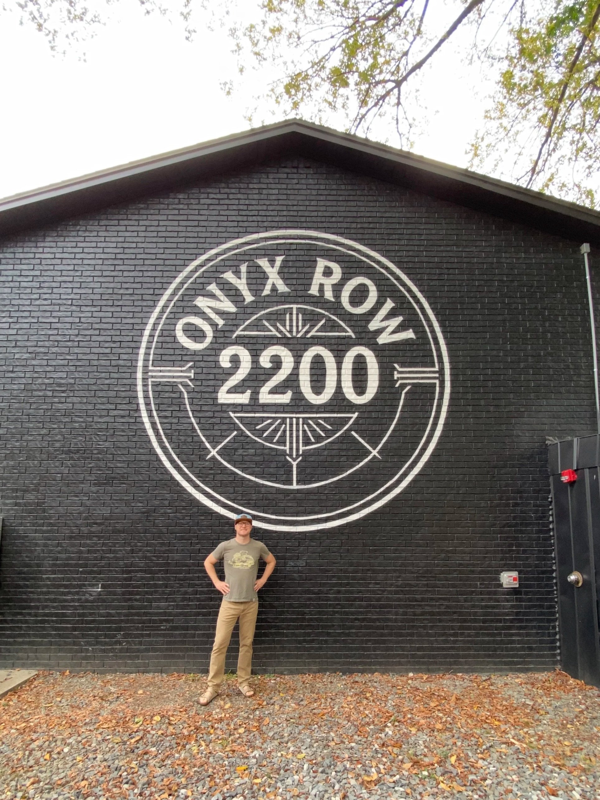 Circular logo mural for Onyx Row Apartments and artist Joel Boyd standing in front
