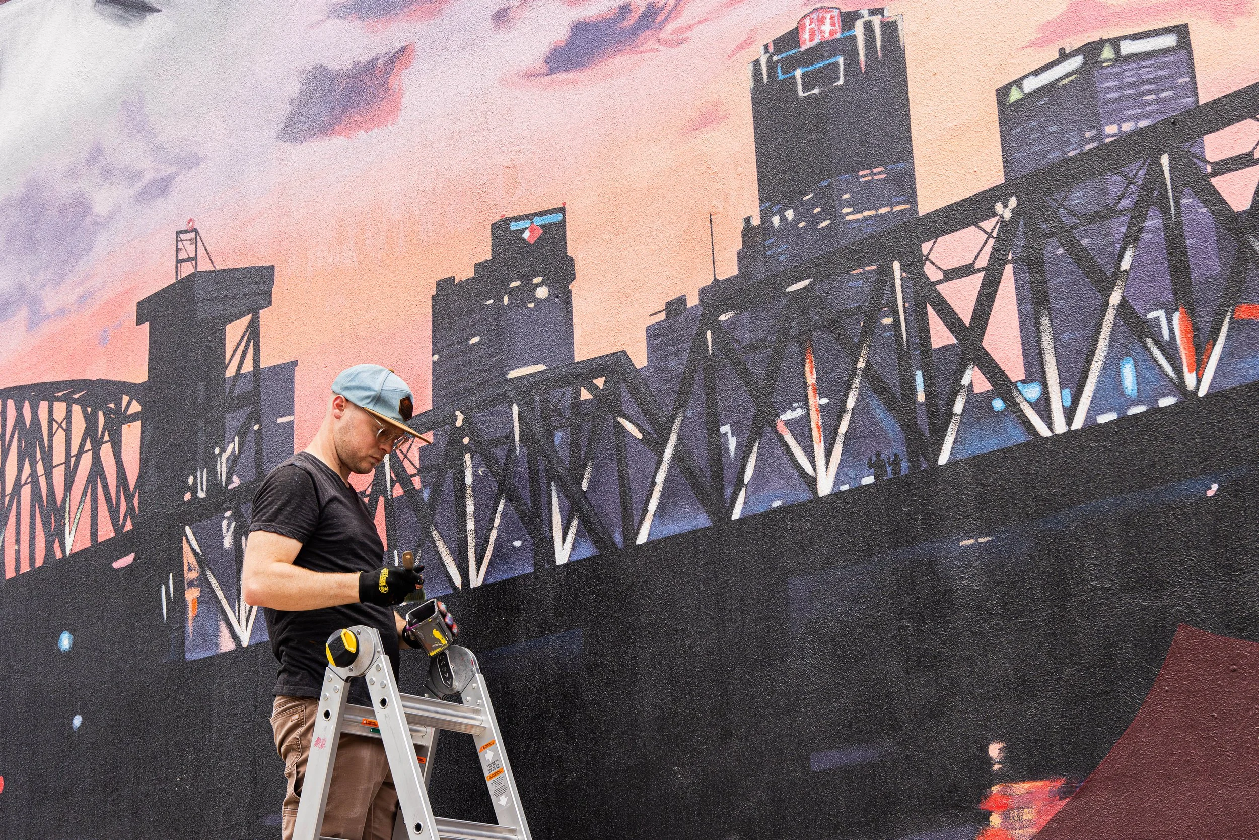 Joel Boyd painting City Dreamers Mural while on Ladder
