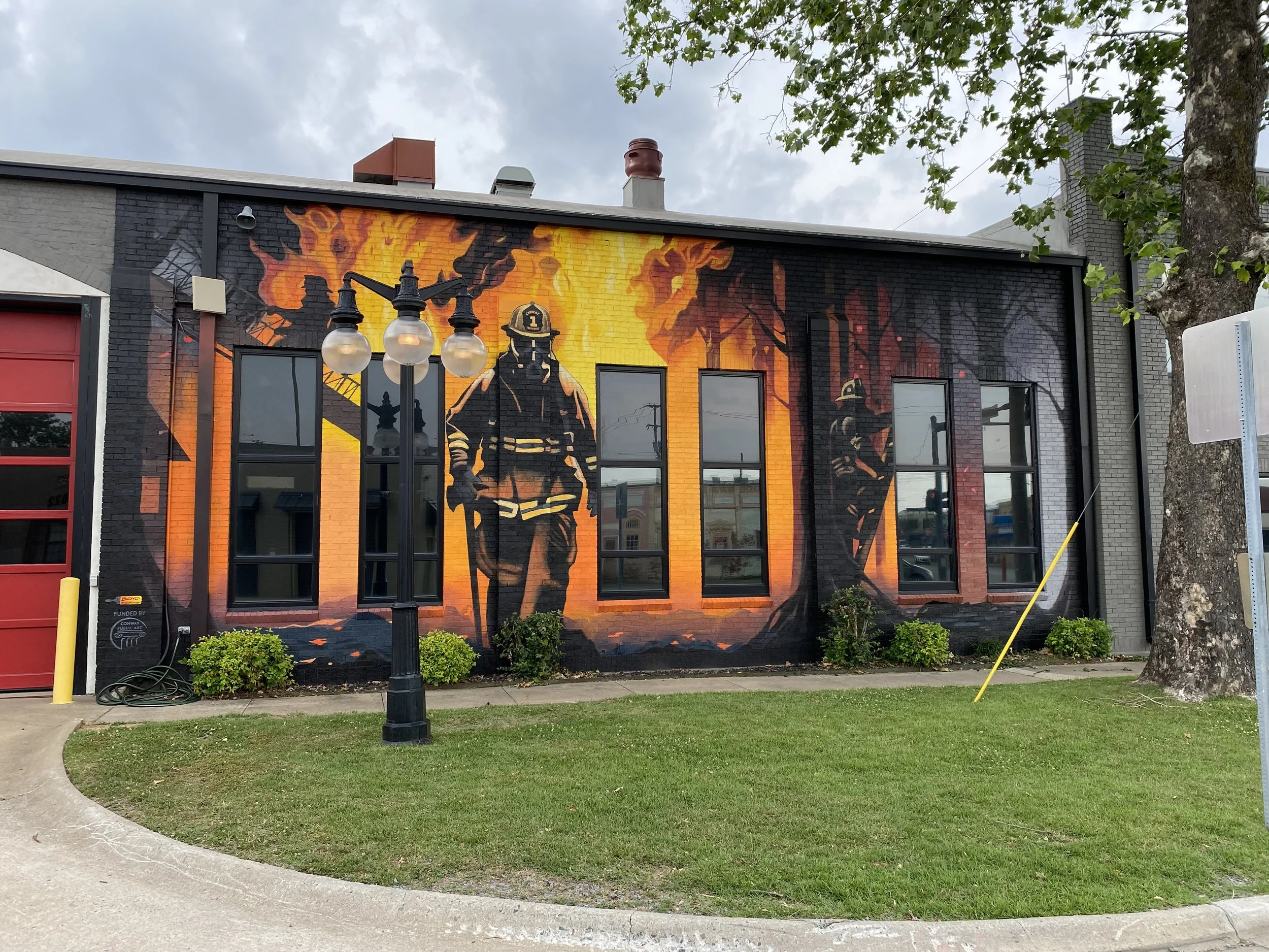 Mural of a firefighter coming with large flames behind him as a mural on a building.
