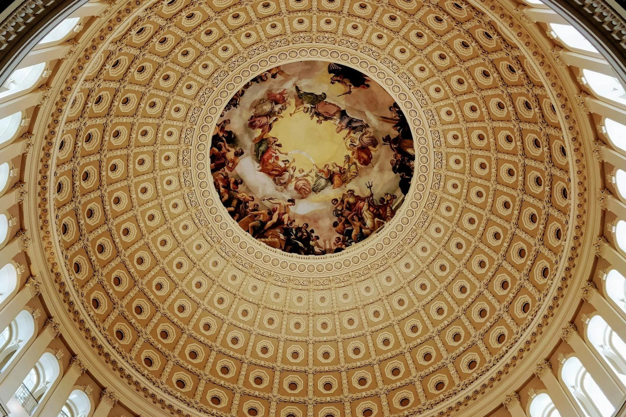Inside view of a domed ceiling with a large painted fresco in the center surrounded by ornate architectural details.