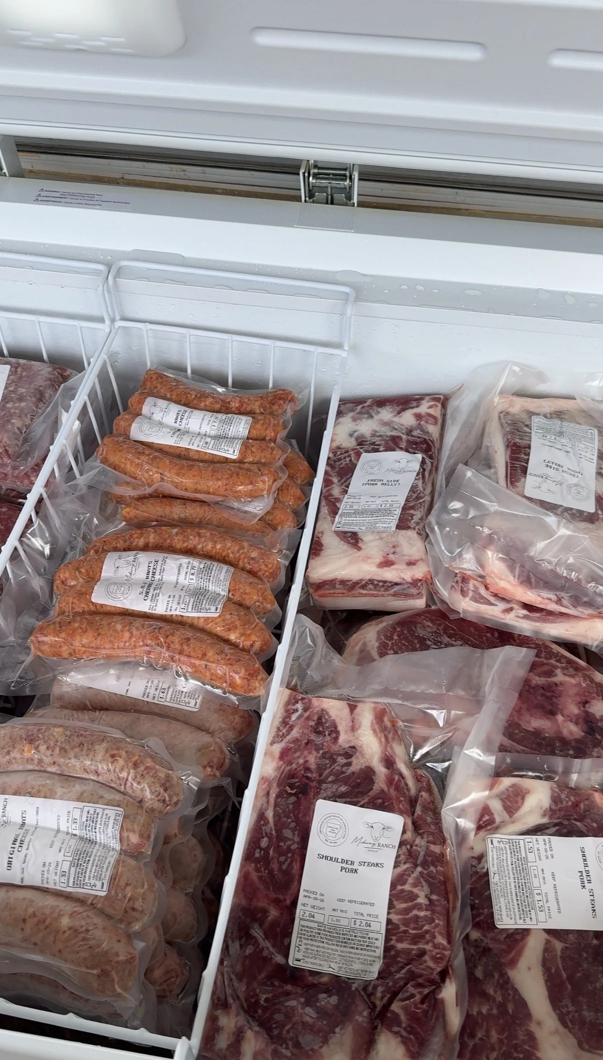 Frozen packages of assorted meats in a meat freezer, including sausages and steaks, with labels indicating types such as shoulder steaks and pork.
