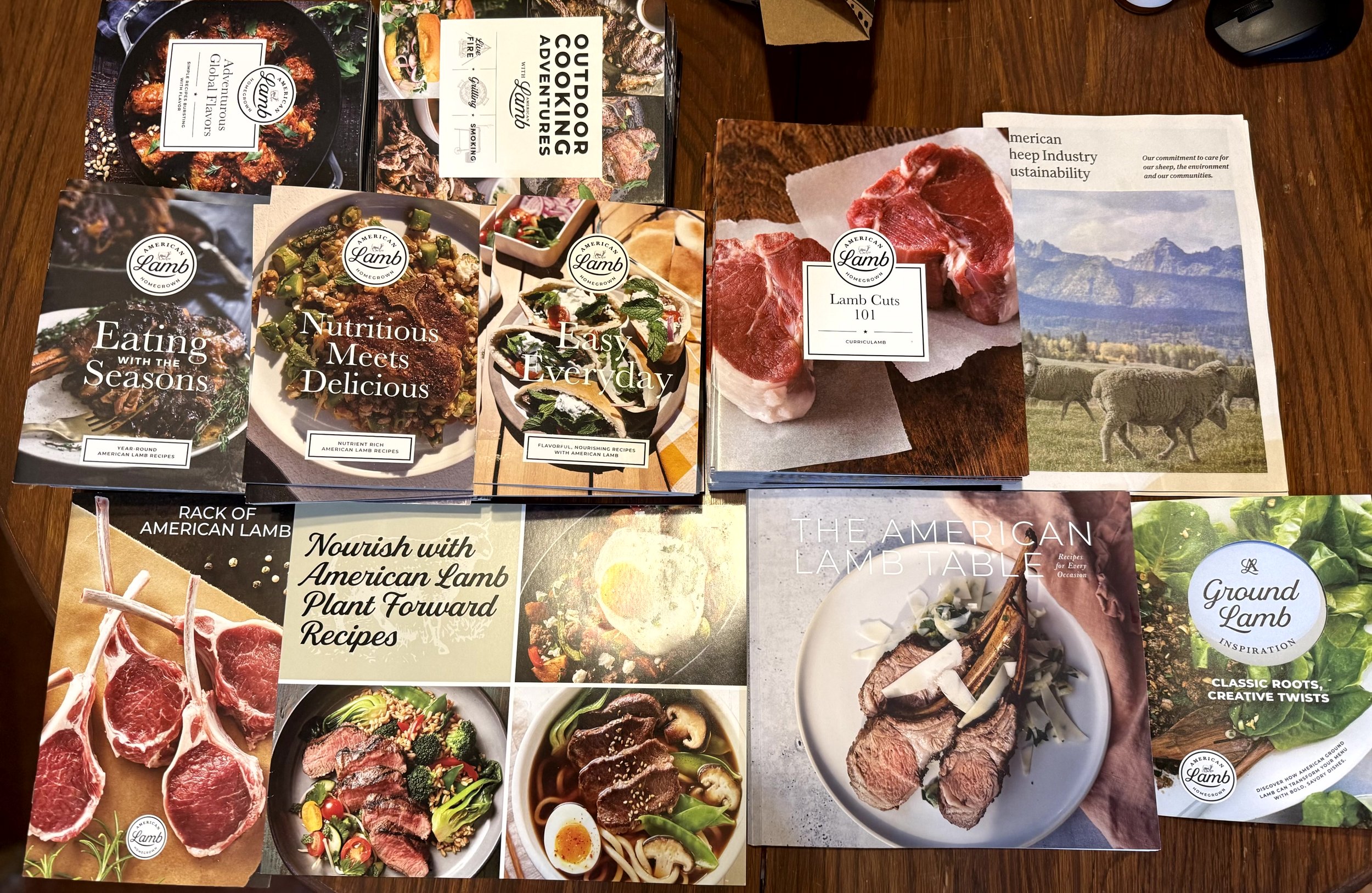 Multiple brochures and booklets about American lamb, including recipes, cooking guides, and information on lamb cuts, displayed on a wooden surface.