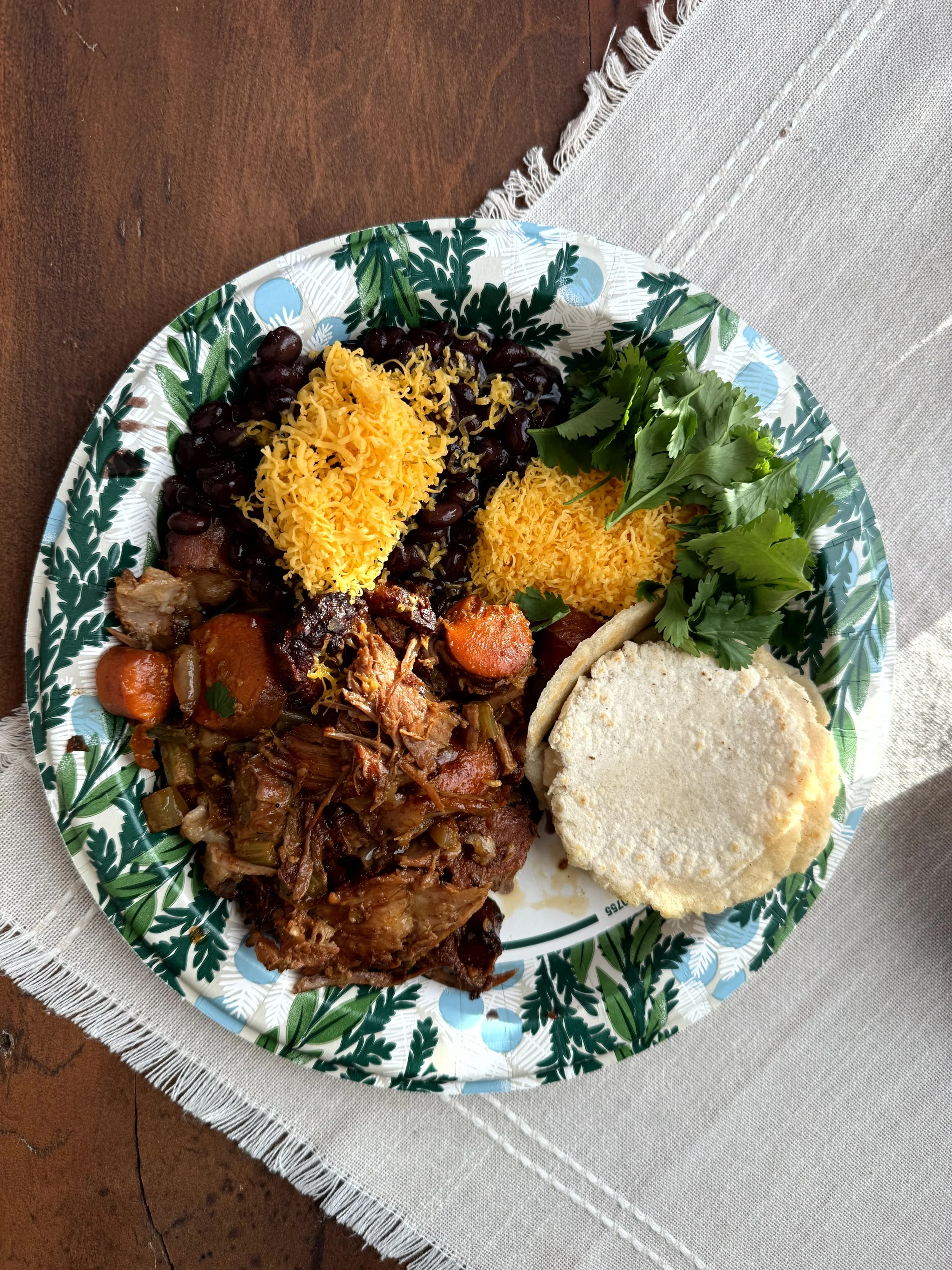 Plate of barbecue baked beans, rice, cornbread, collard greens, and cooked vegetables on a green and white patterned disposable plate.