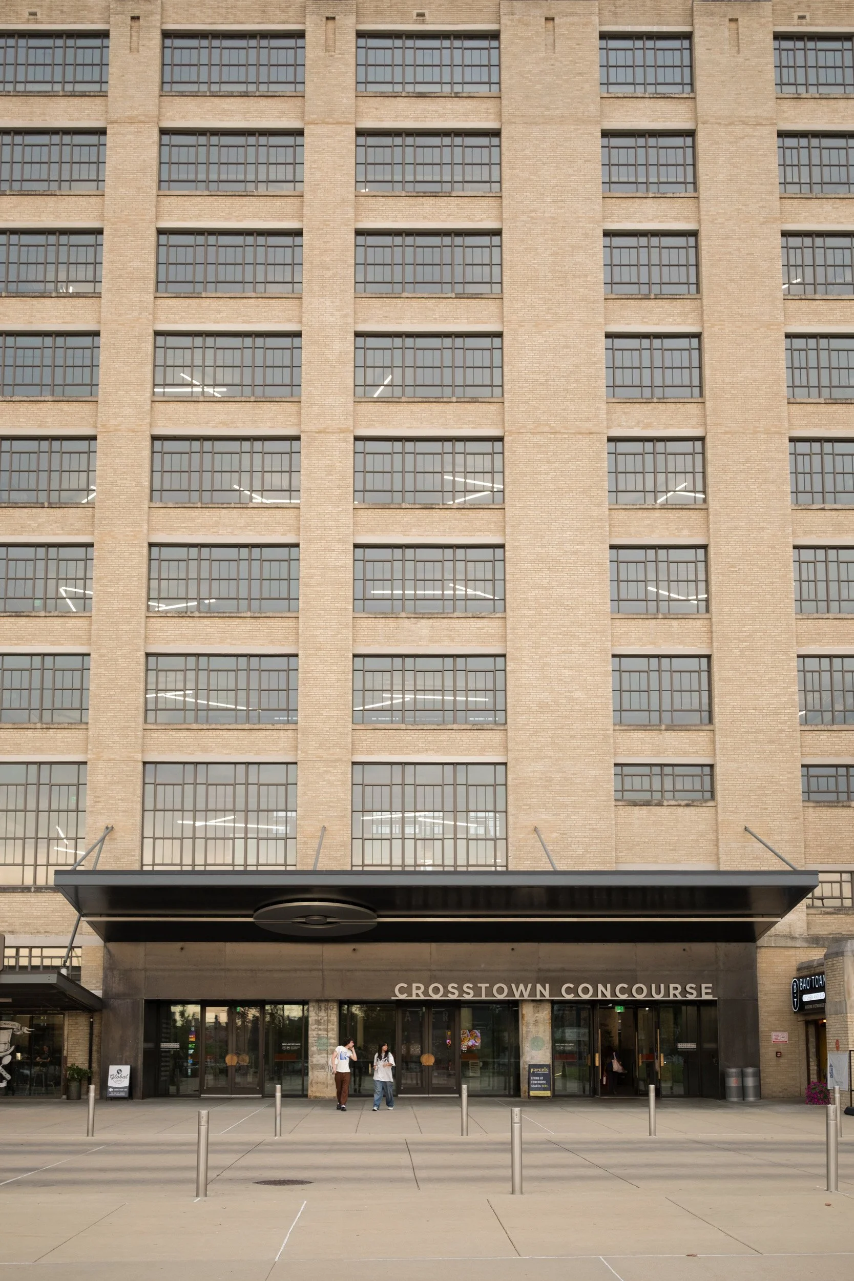 Facade of a building with lots of large windows and a sign for Crosstown Concourse at the entrance, with a few people walking in front.