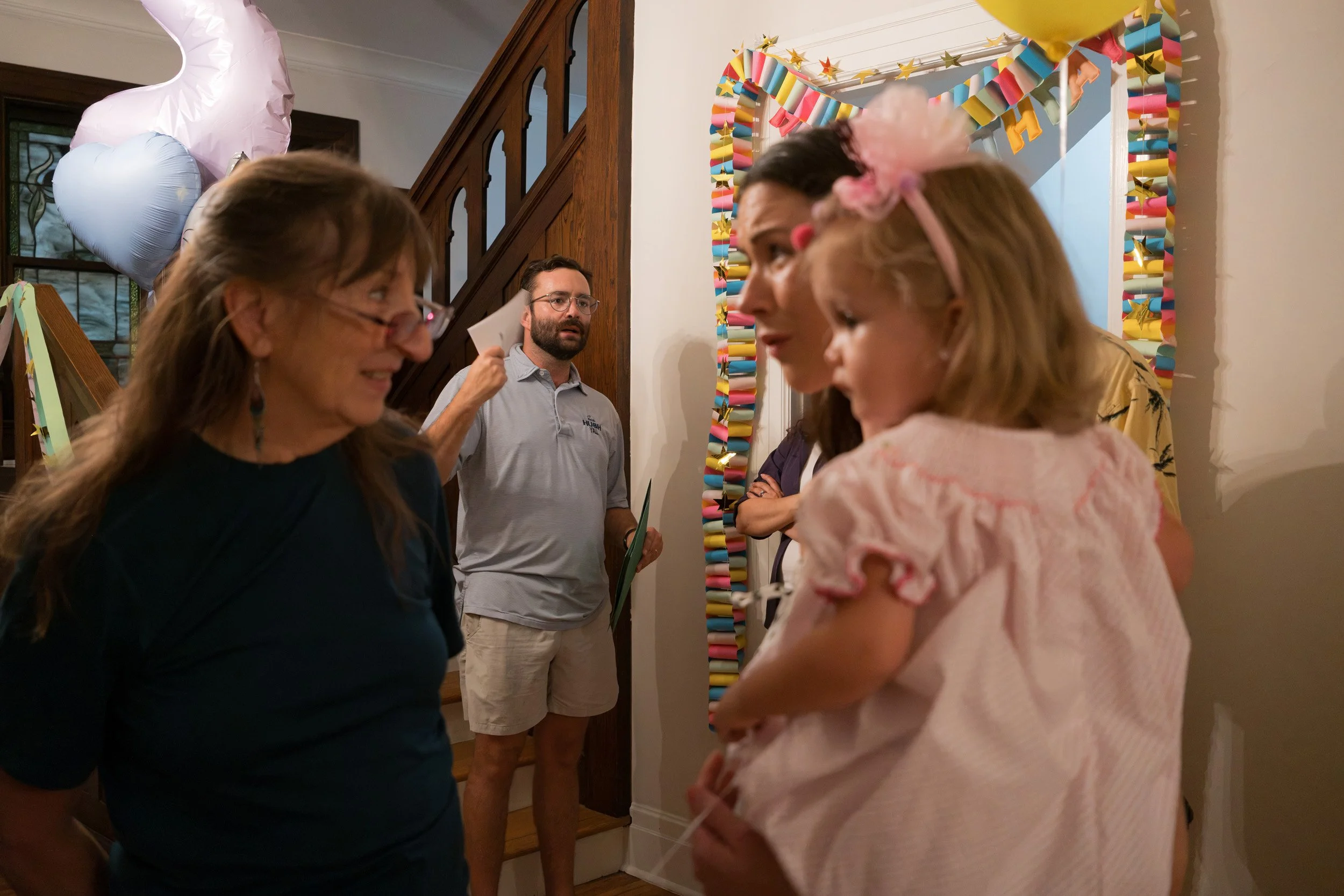 A group of people gathered at a party, decorated with colorful streamers and balloons, engaging in conversation.
