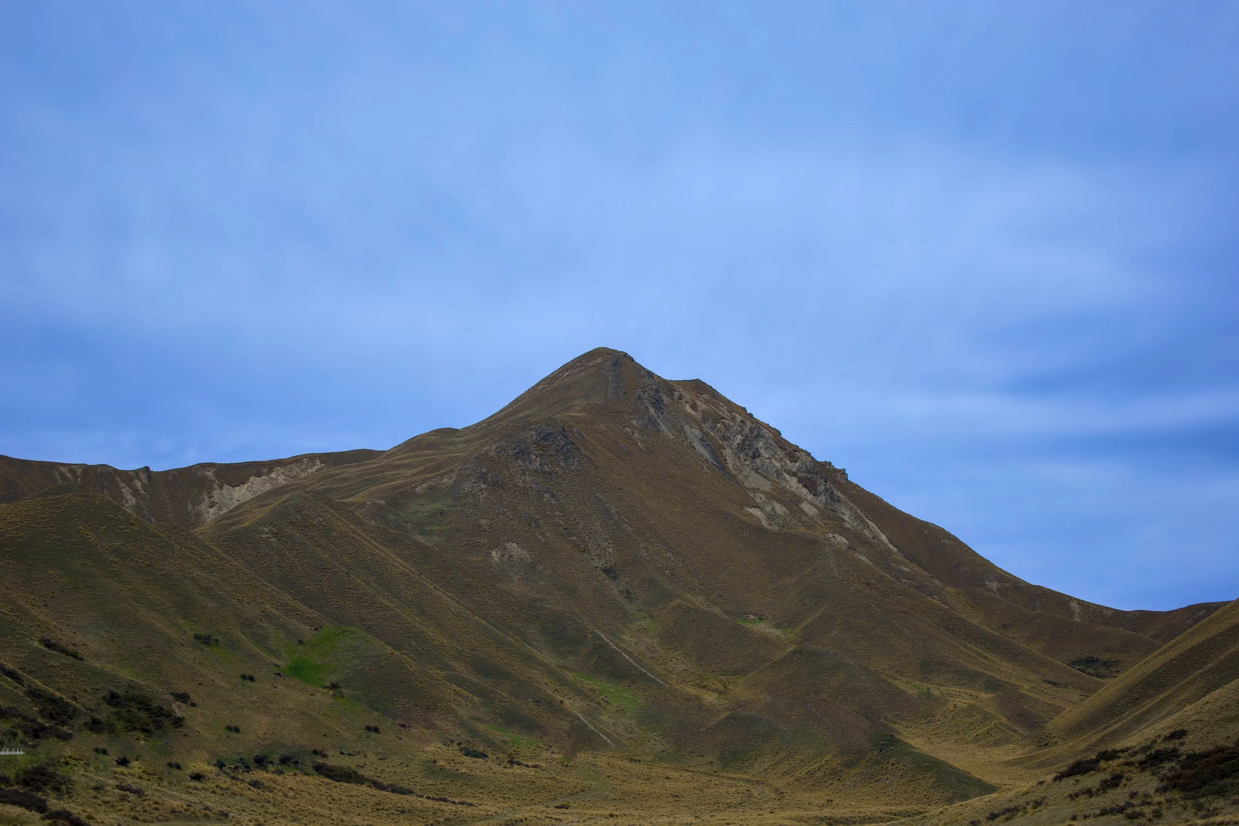 A mountain with ridges and slopes, under a blue sky with sparse clouds.