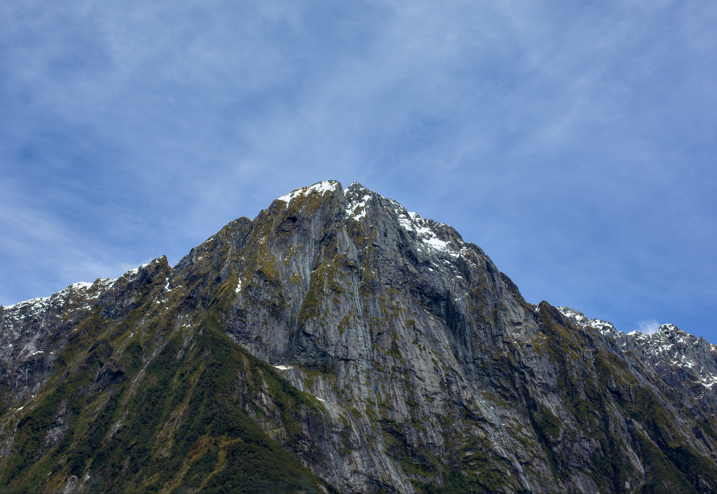 Snow-capped mountain peak under a blue sky with wispy clouds.
