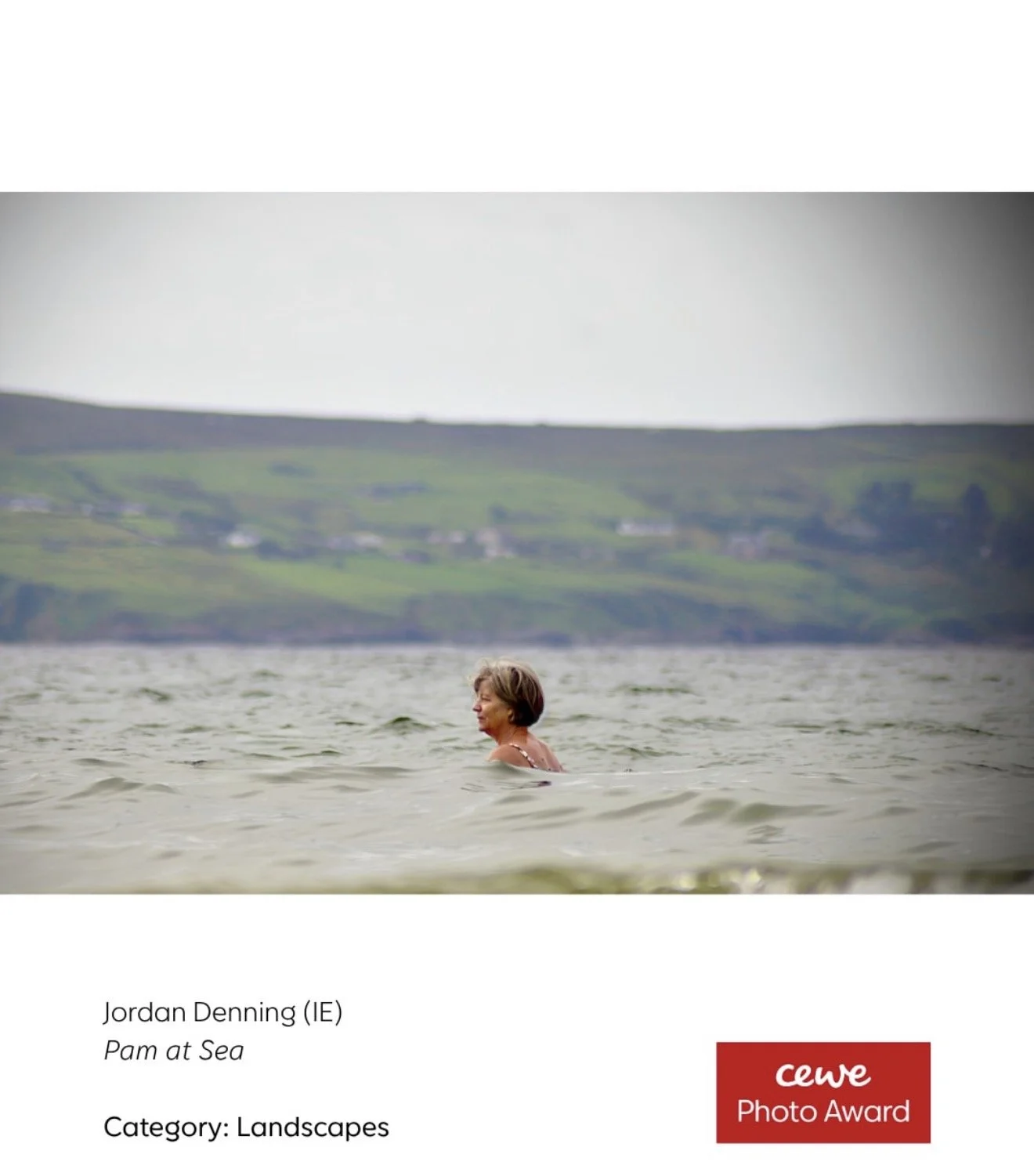 A woman swimming in a body of water with a hilly landscape in the background.