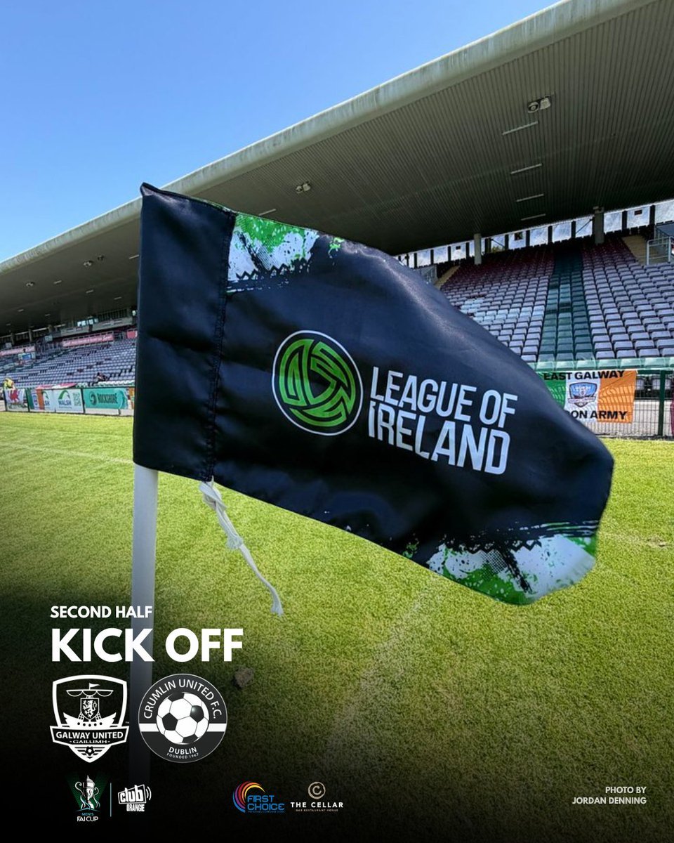A soccer field corner flag with League of Ireland logo, with empty stands in the background, indicating second-half kickoff of a match between Galway United and Crumlin United.