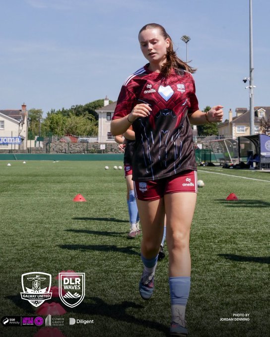 Female rugby player in a maroon and black jersey running on a rugby field.