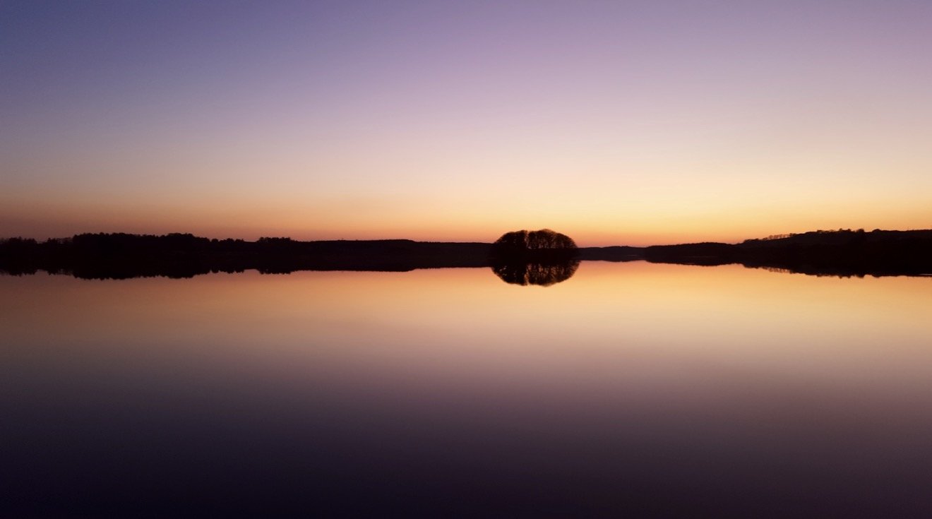 Sunset over a calm lake with a silhouette of trees reflected on the water