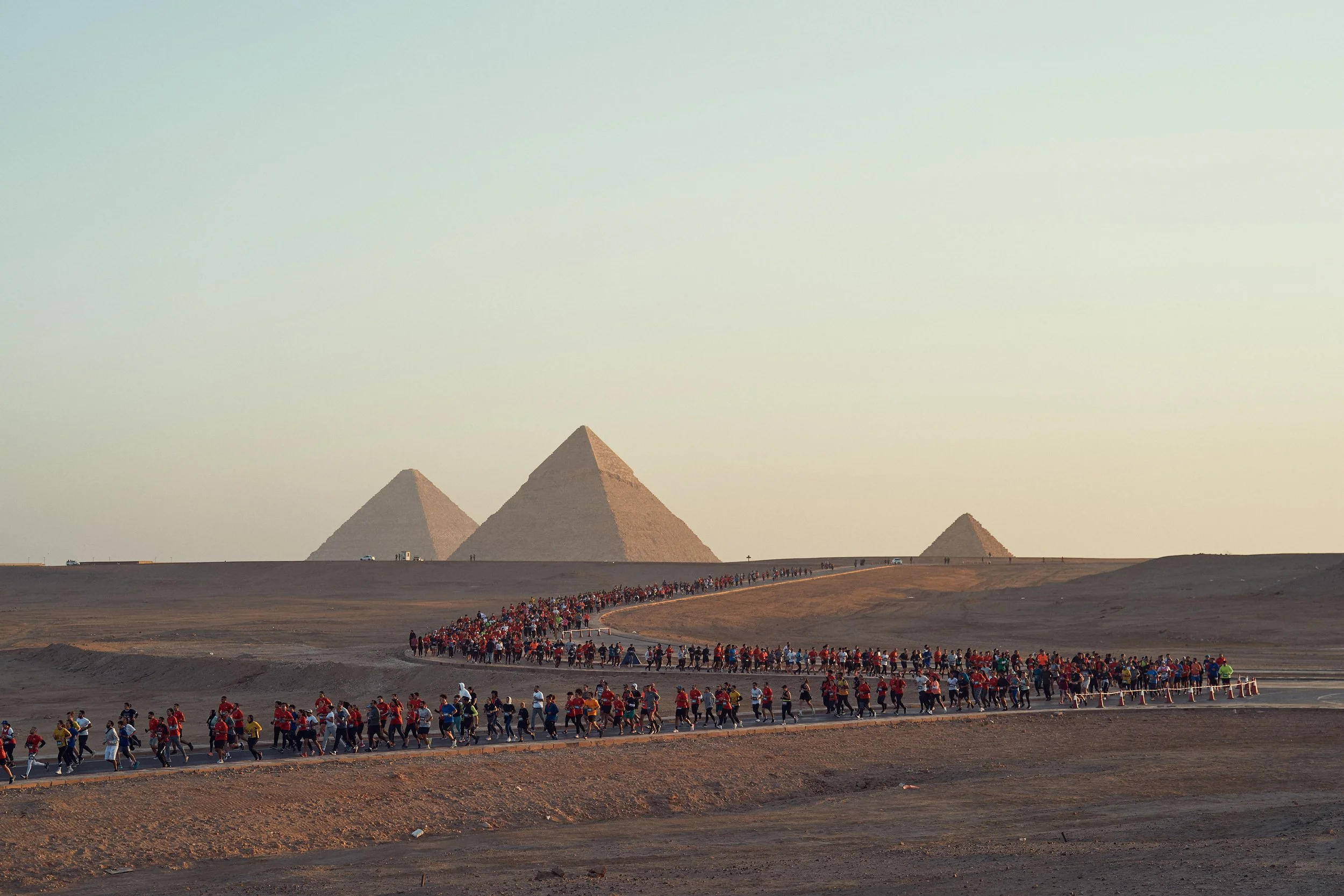 People walking in a long line near the Pyramids of Giza during sunset or sunrise.