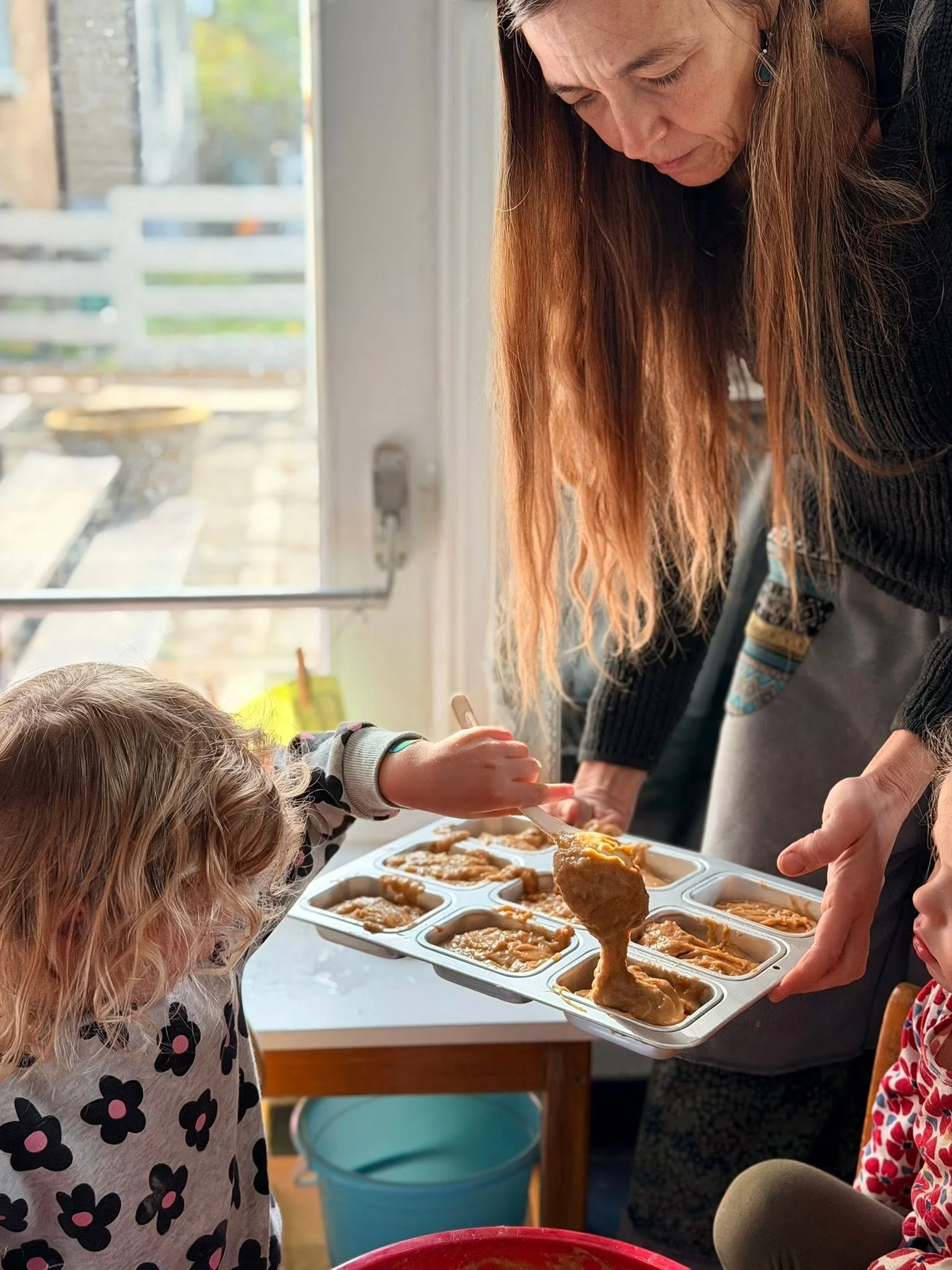 A woman is serving food into a mold with compartments that contain mashed sweet potatoes, during a community meal or gathering, with a child in a floral shirt reaching out for food.