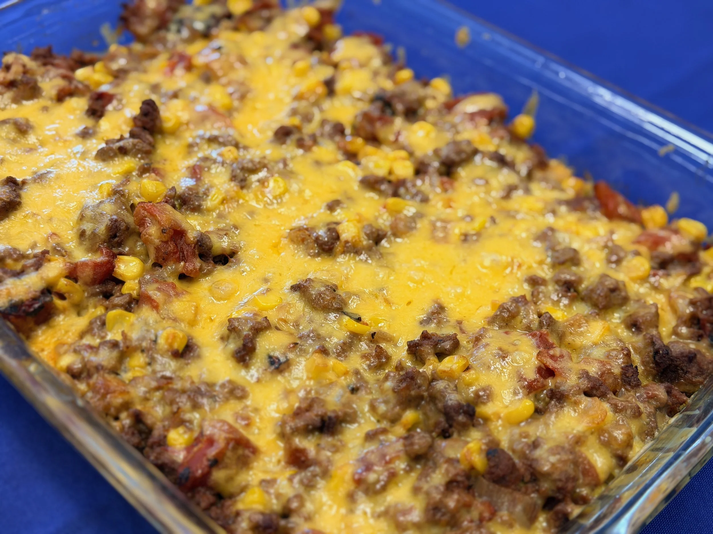 Baked casserole dish with ground beef, corn, tomato, and melted cheese in a glass dish.