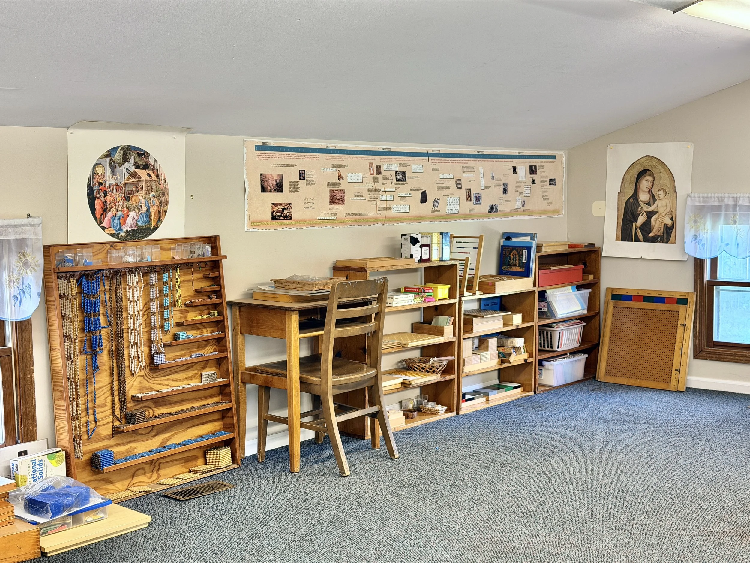 A classroom or study room with educational posters, bookshelves, and religious imagery, including depictions of religious figures and scenes.