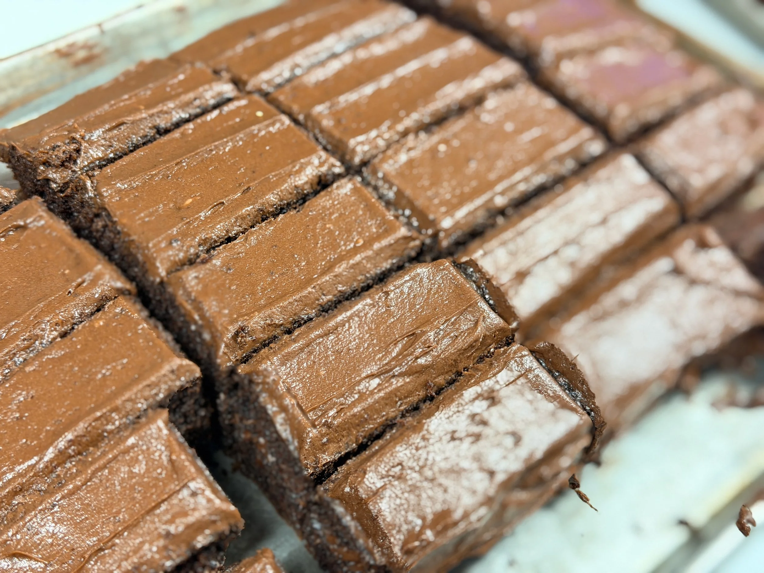 Close-up of sliced chocolate fudge on a glass tray, with a dusting of powdered sugar.